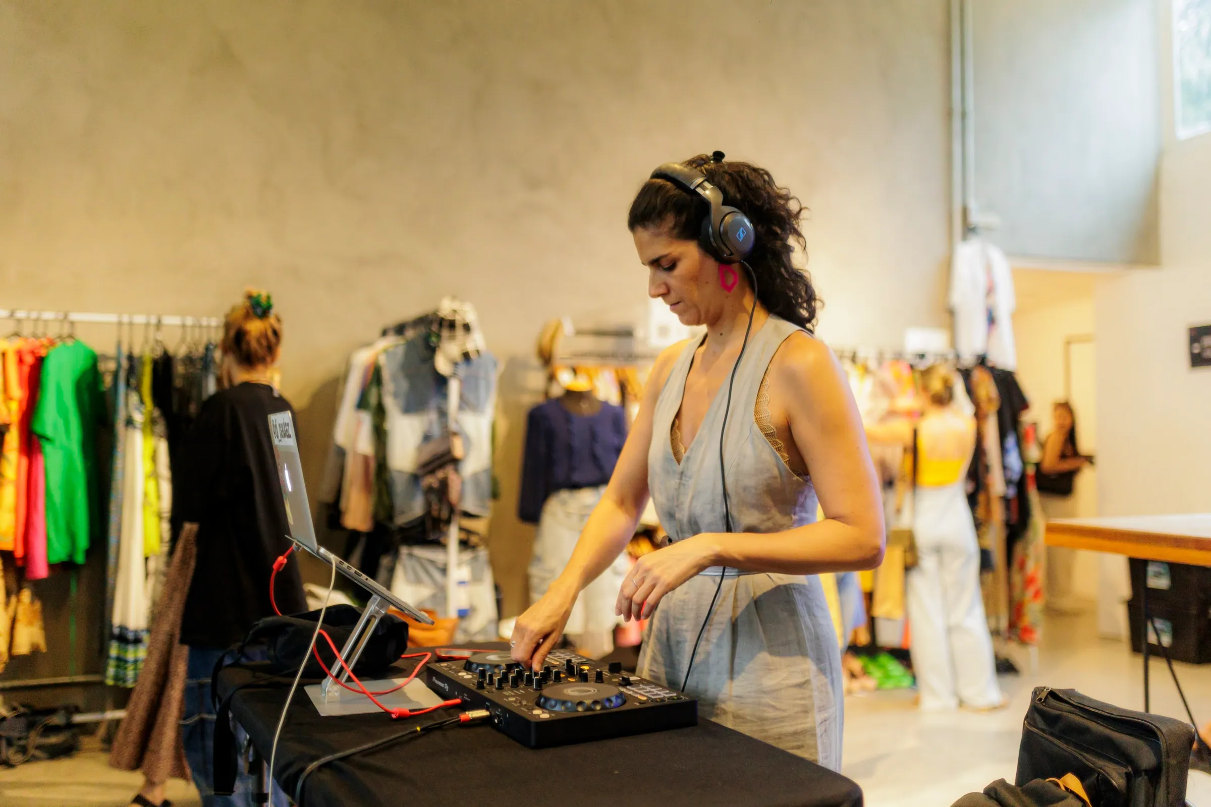 DJ toca em pick-up dentro de um brechó com araras de roupas coloridas ao fundo, evento de garimpo na Casa Cósmica