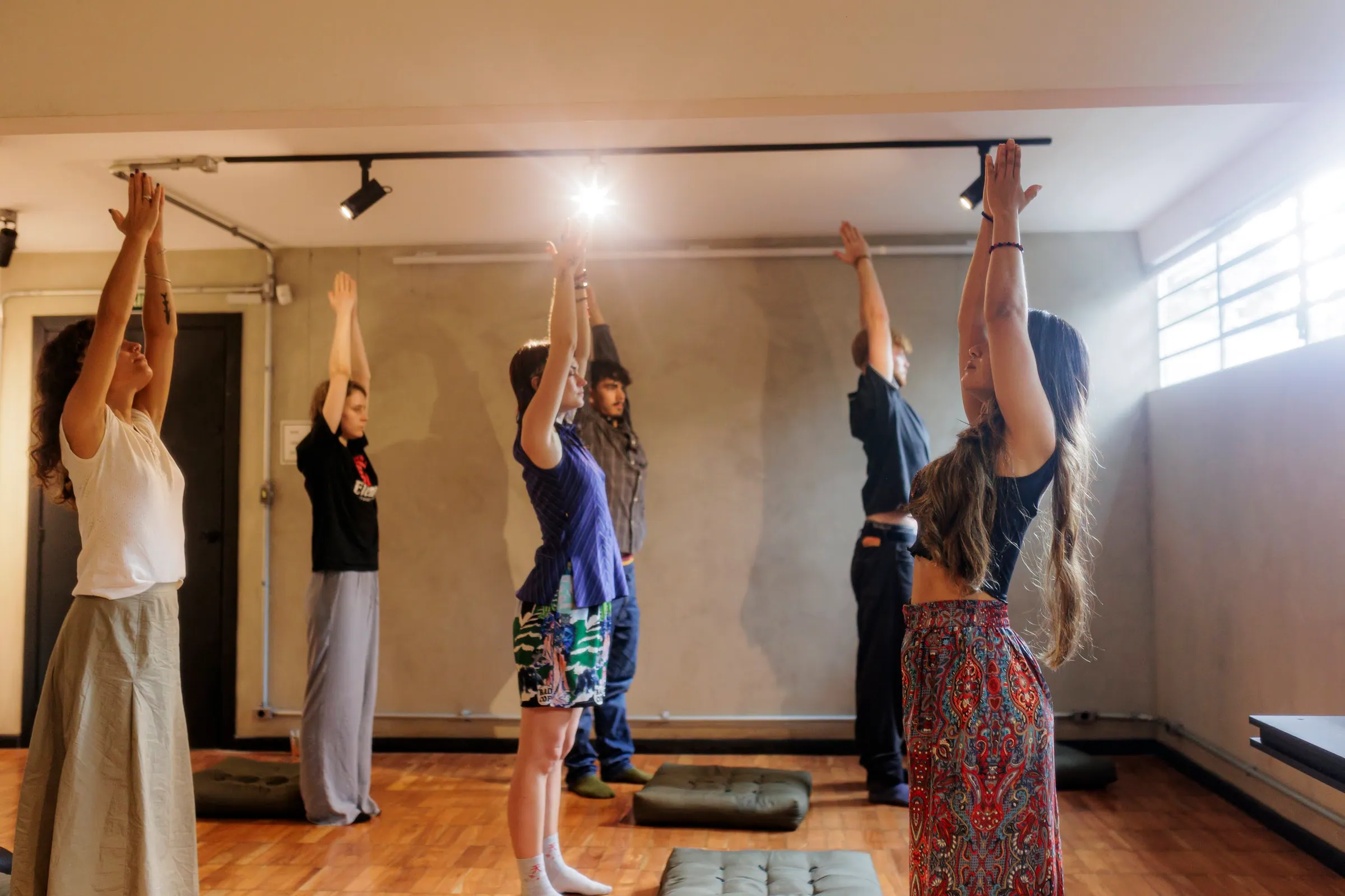 Turma de yoga em pé com os braços erguidos, luz da manhã entrando pela janela