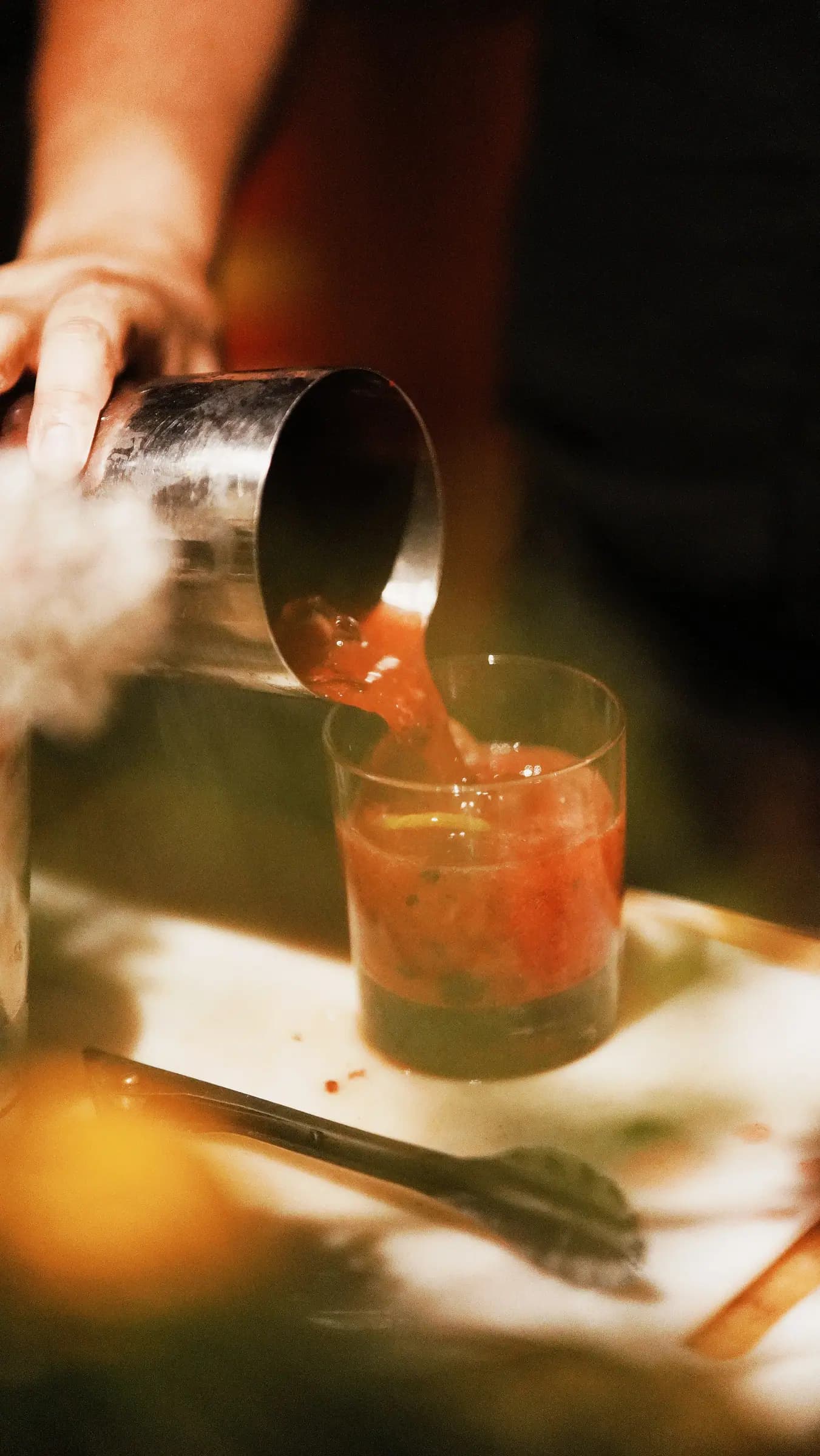 Bartender servindo drink vermelho em copo sobre a mesa, luz da tarde