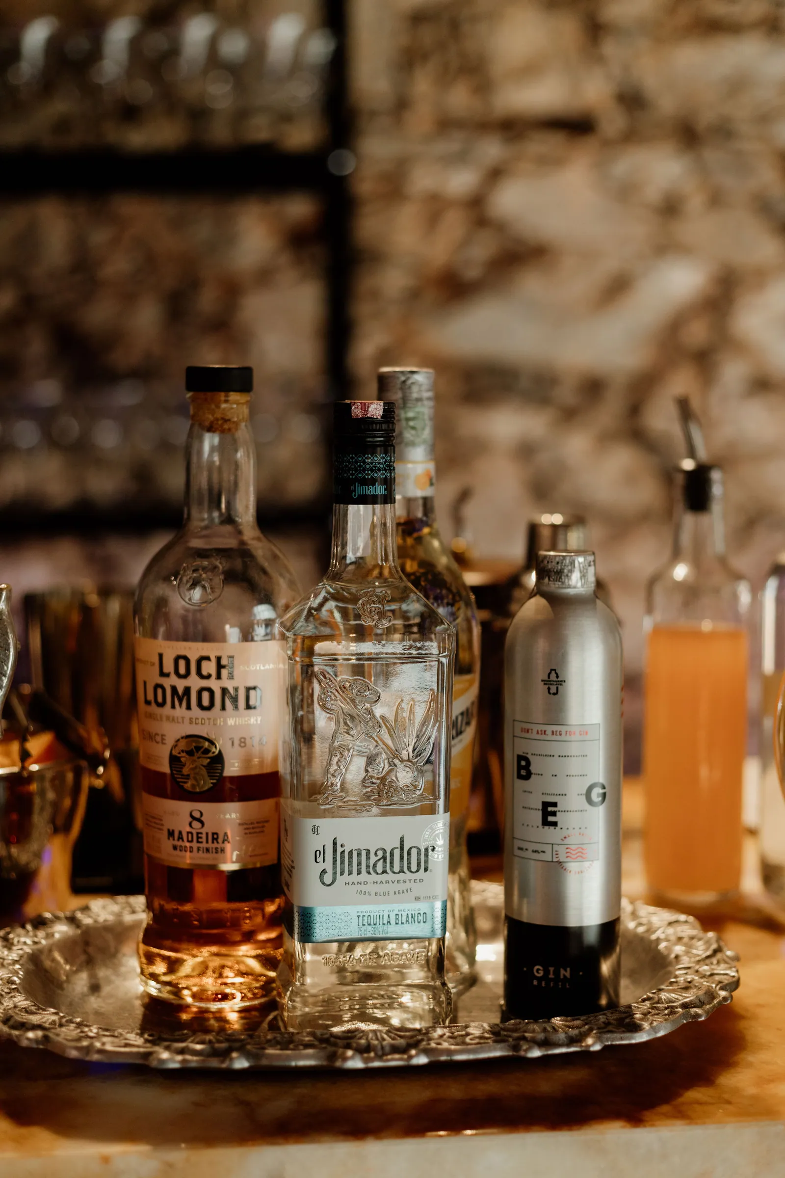 Garrafas de whisky, tequila e água tônica dispostas em bandeja de prata
