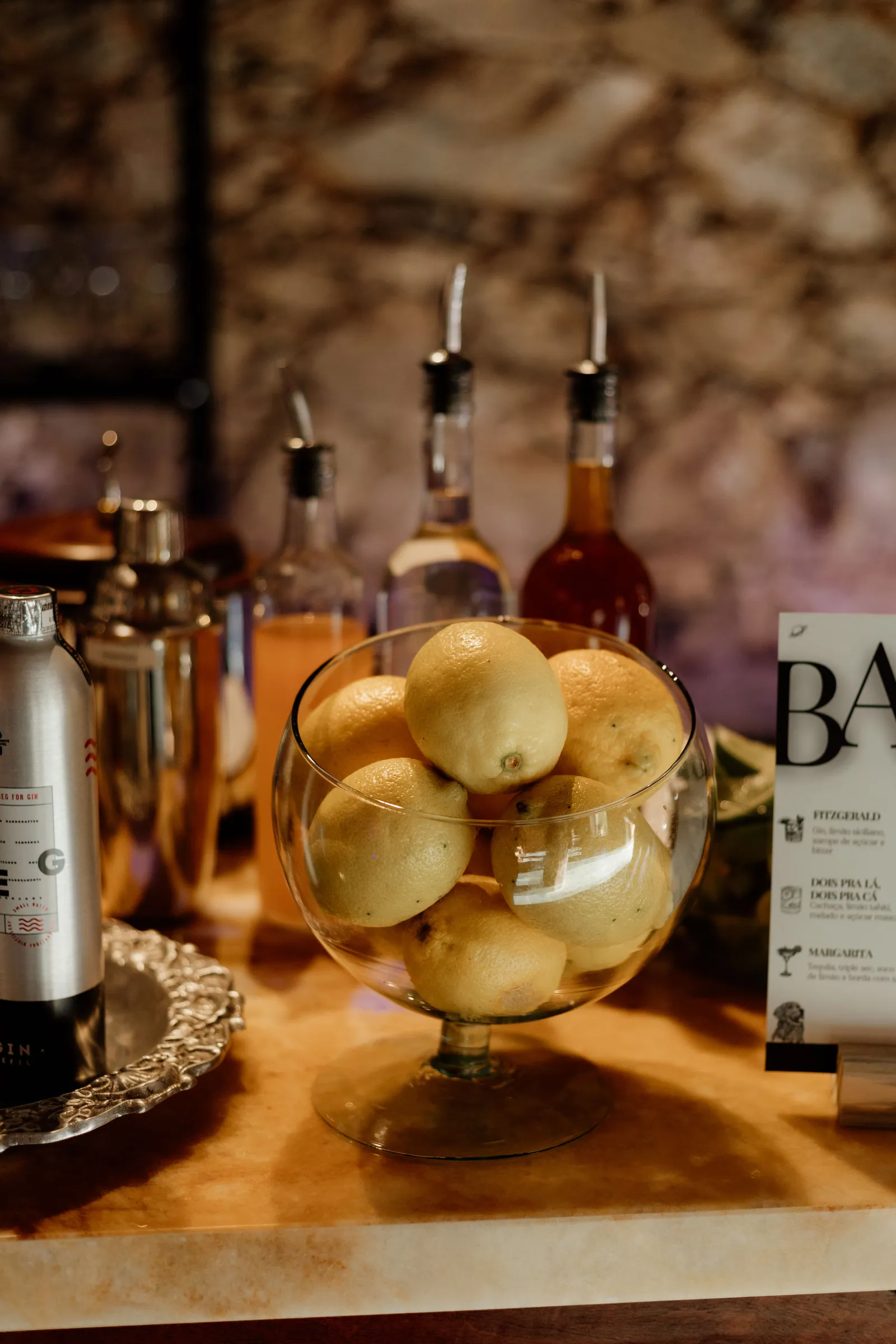 Bandeja com garrafas de destilados e taça de limões-sicilianos sobre a bancada