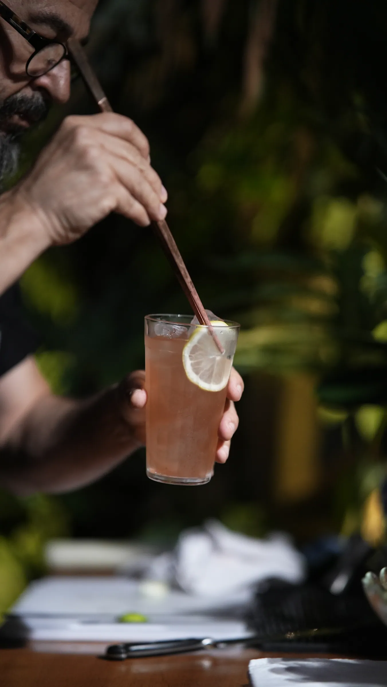 Bartender mexendo um drink com colher longa, copo com rodela de limão