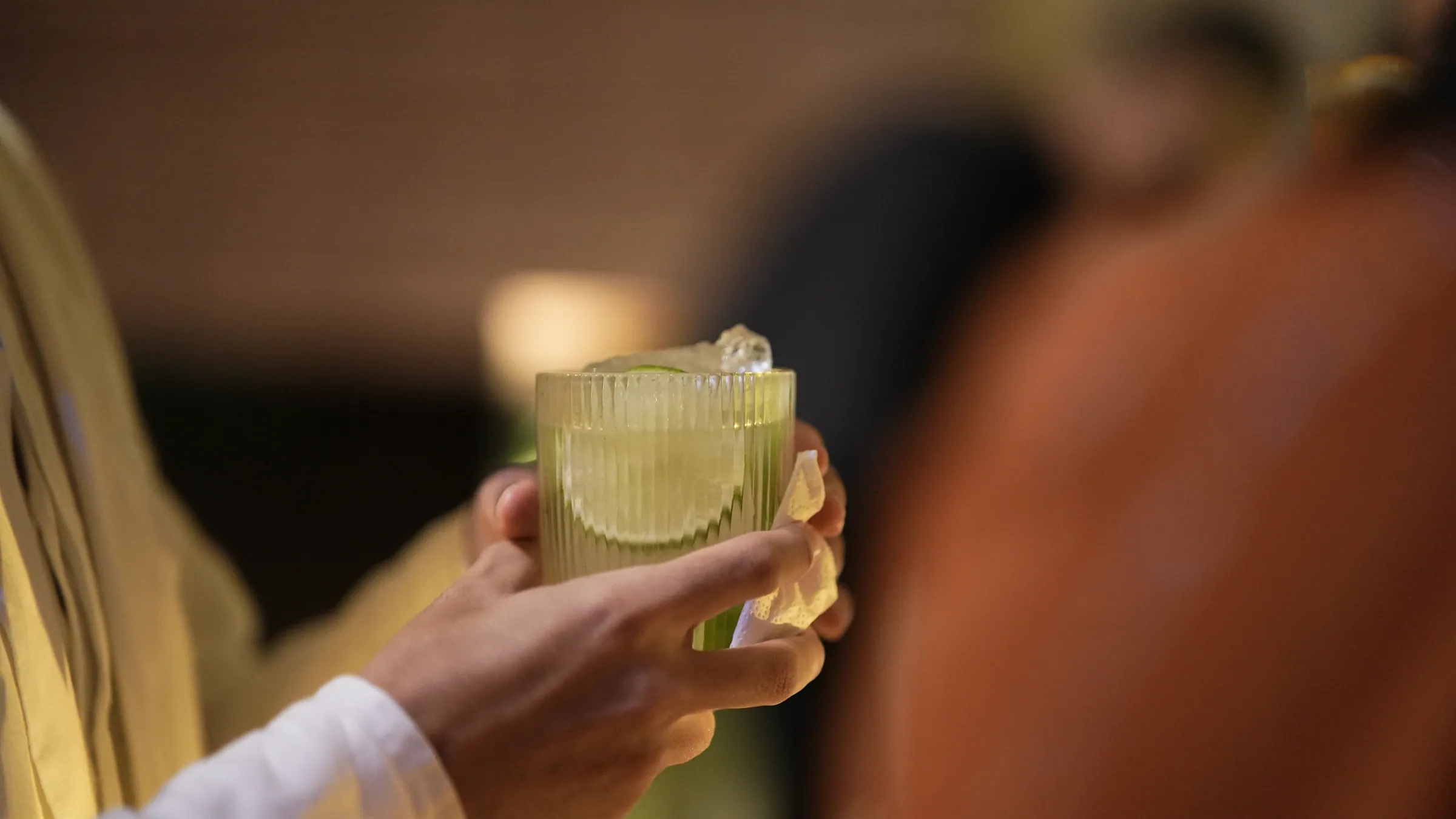 Convidada segurando copo de drink claro com guarnição, luz quente de fim de tarde