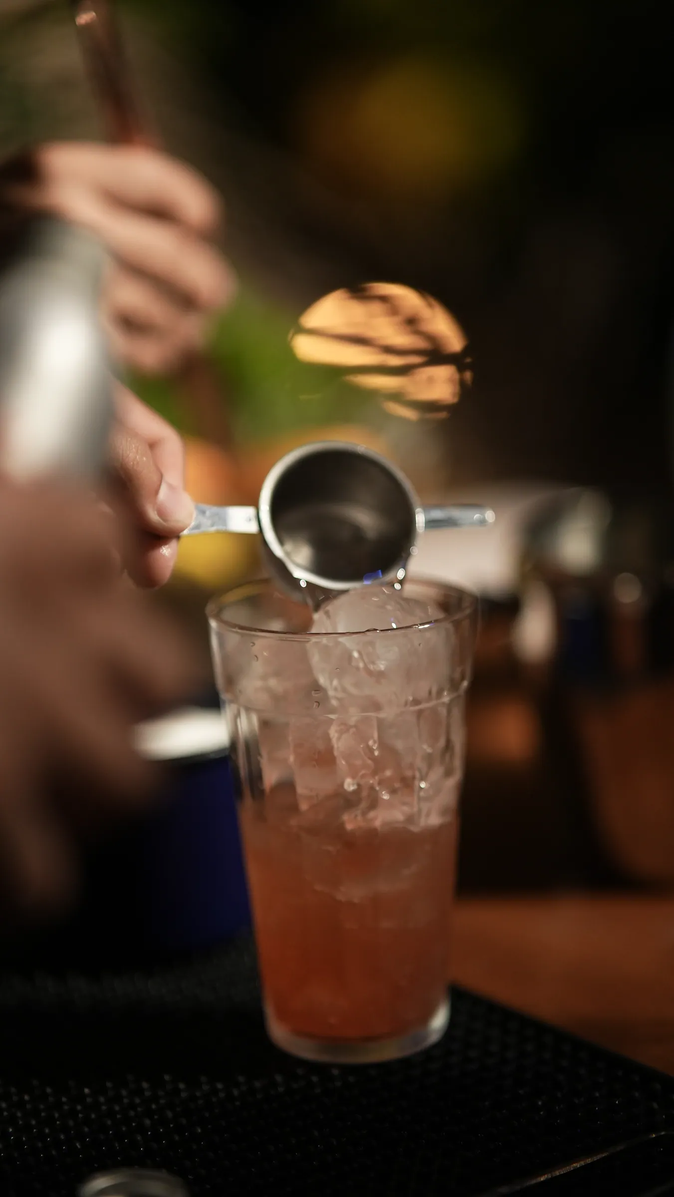 Bartender dosando bebida com jigger sobre copo com gelo e drink rosado