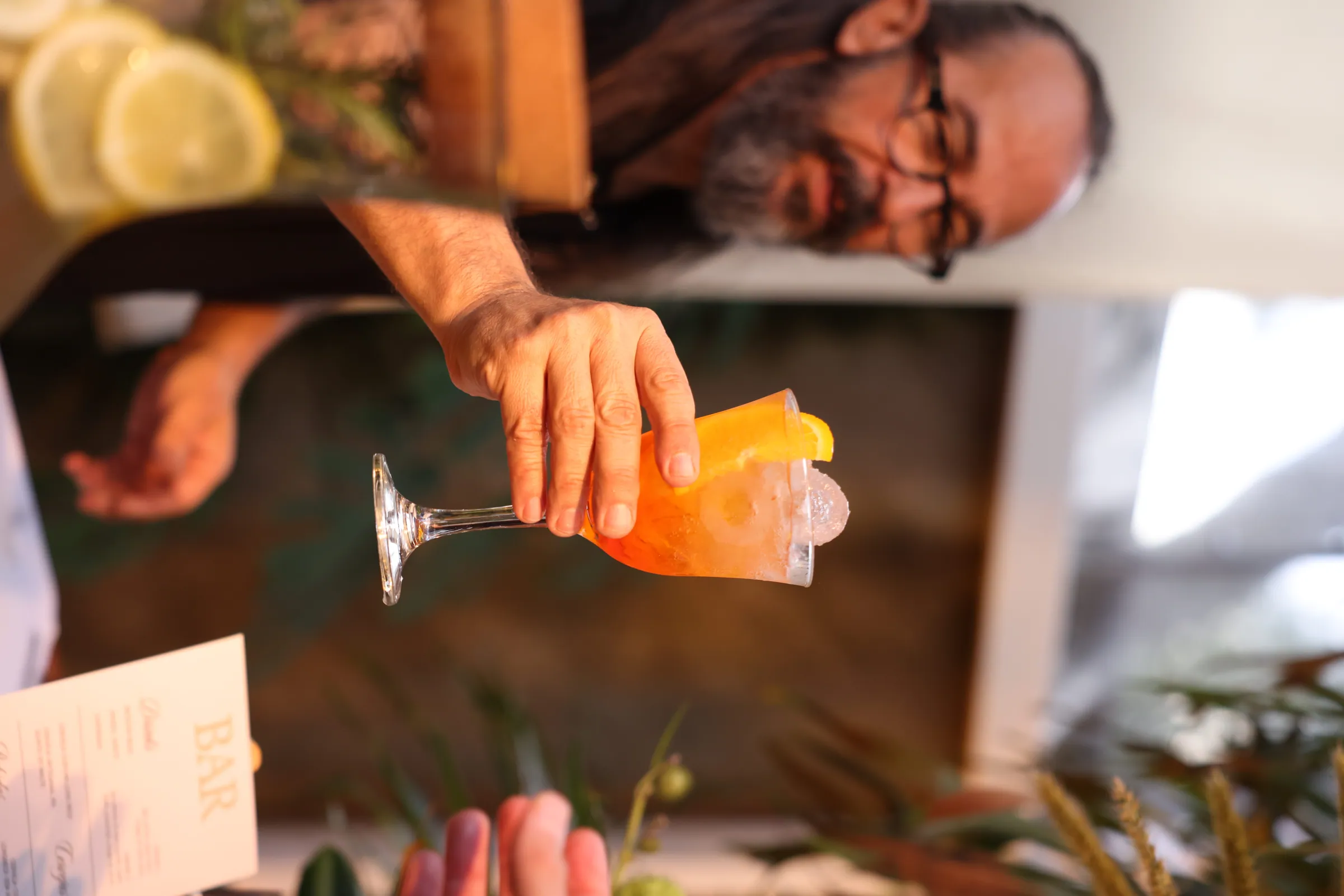 Bartender finalizando um drink com fatia de laranja em taça