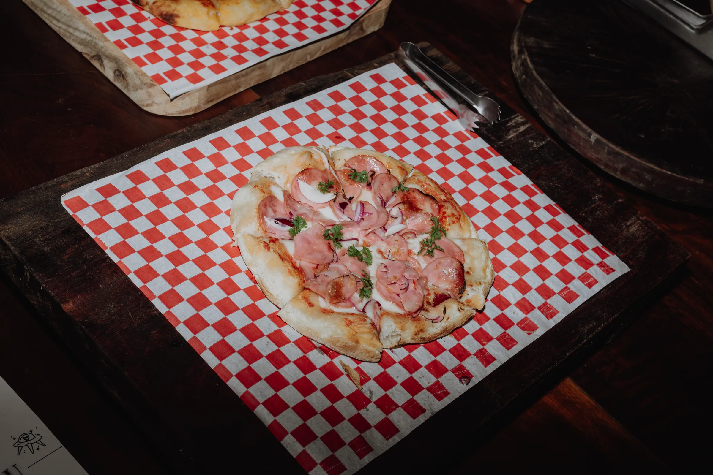 Mini pizza individual de calabresa e cebola roxa sobre papel xadrez vermelho e branco