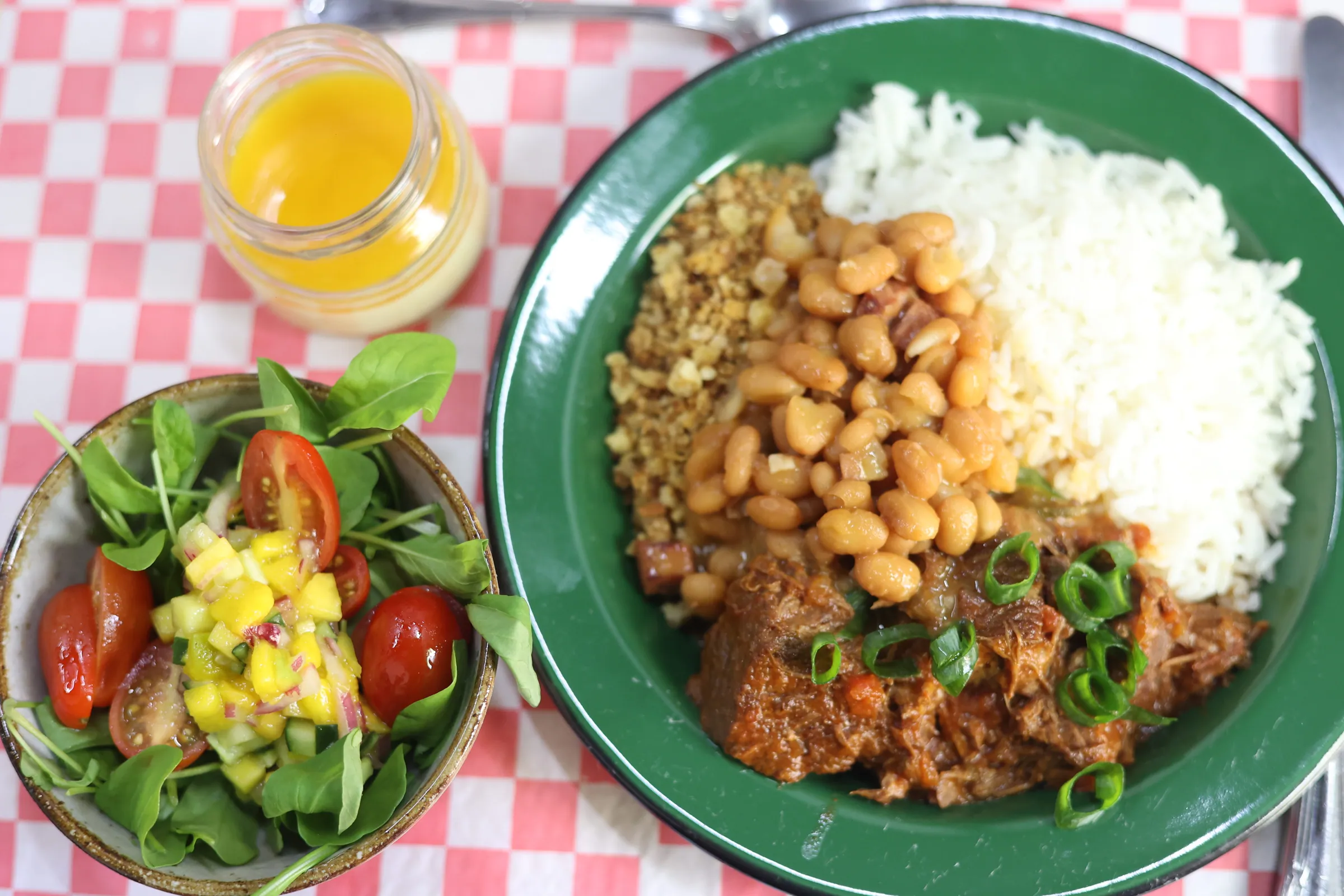 Prato de carne desfiada ao molho com feijão tropeiro, arroz branco e farofa, ao lado de salada verde e suco de laranja