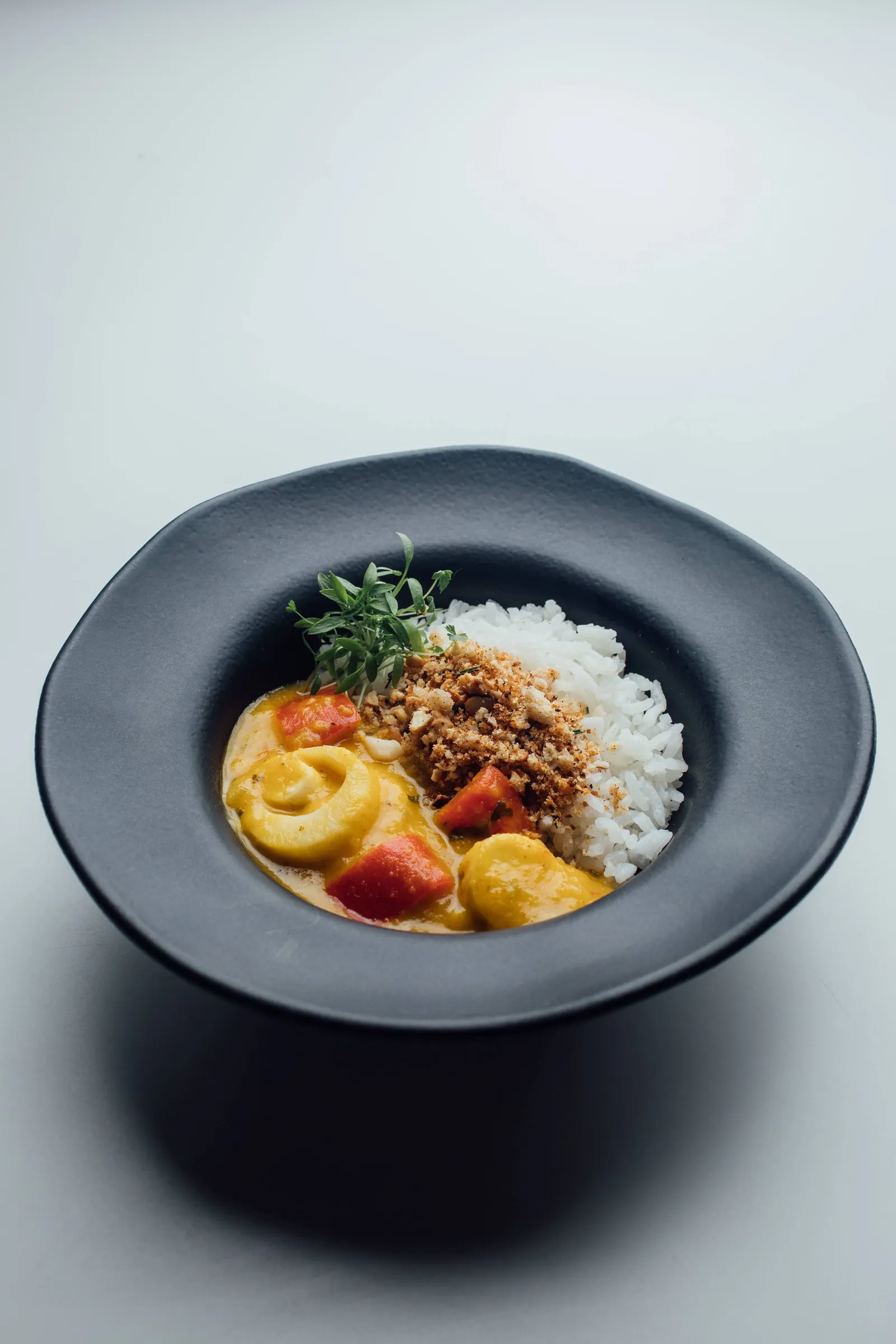 Curry cremoso com legumes e farofa crocante ao lado de arroz branco, servido num prato fundo escuro