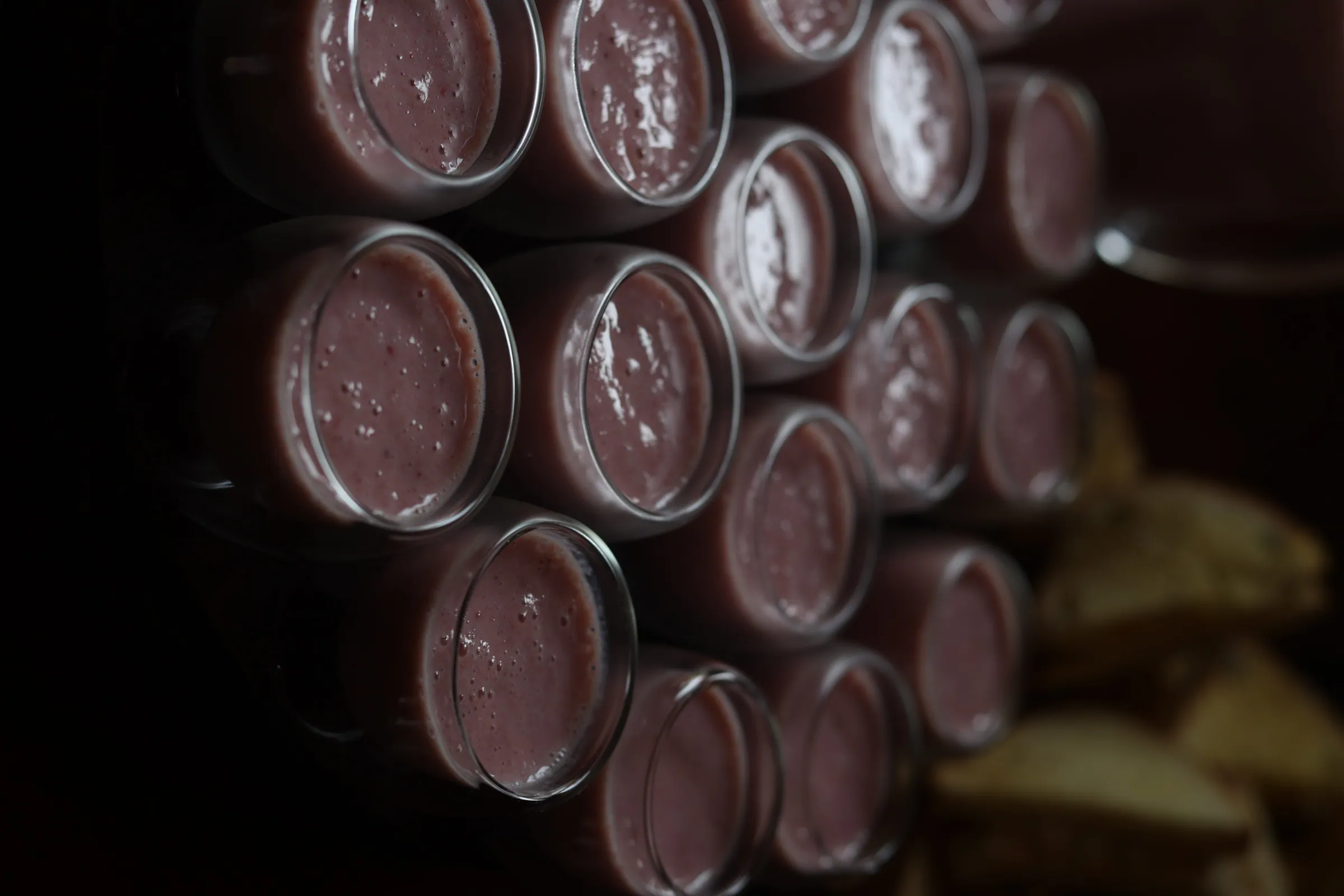 Fileira de potinhos de mousse de chocolate vistos de cima, em ambiente escuro e intimista