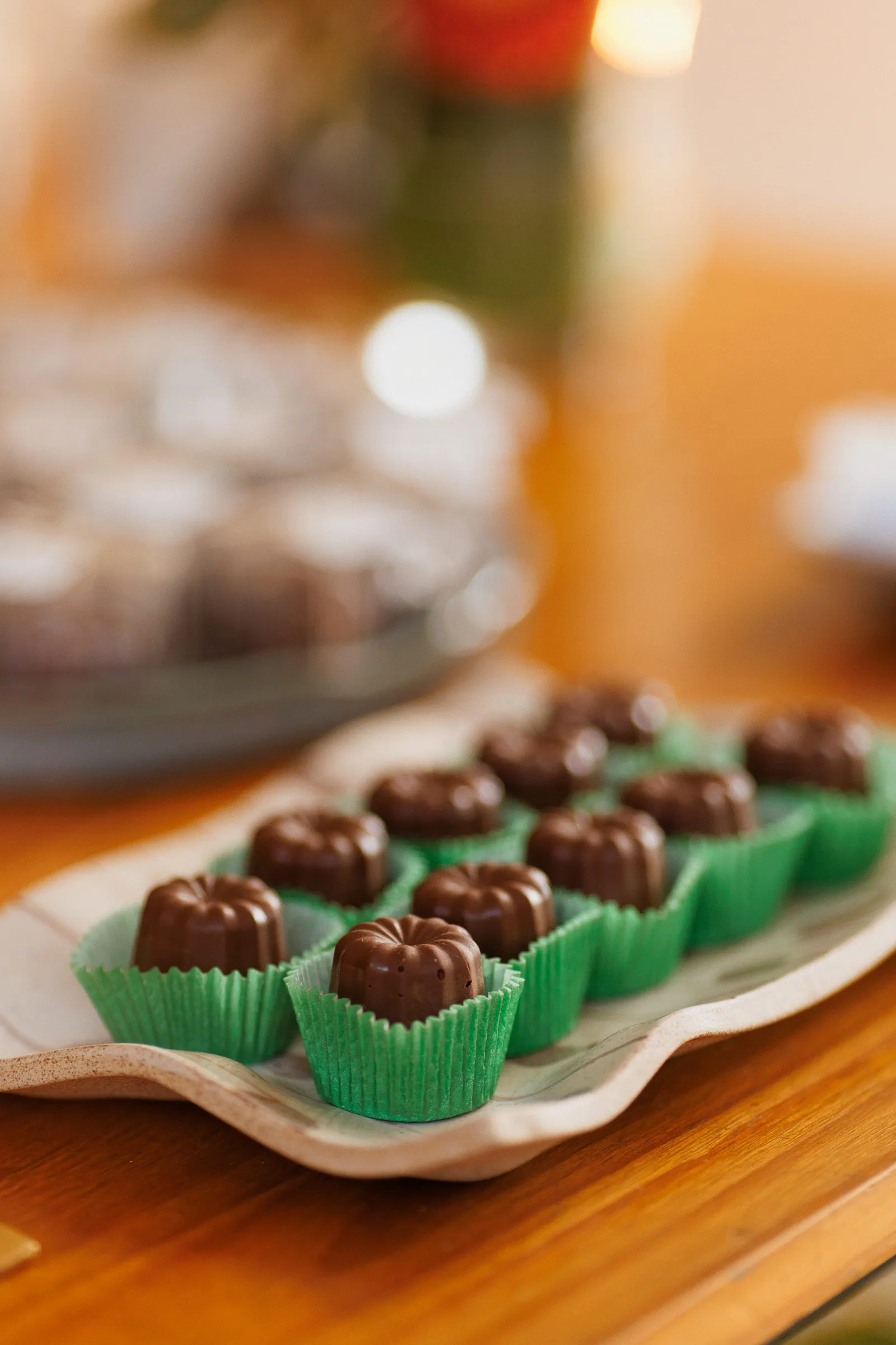 Bombons de chocolate em formato de flor, um em cada forminha verde, servidos numa travessa de festa