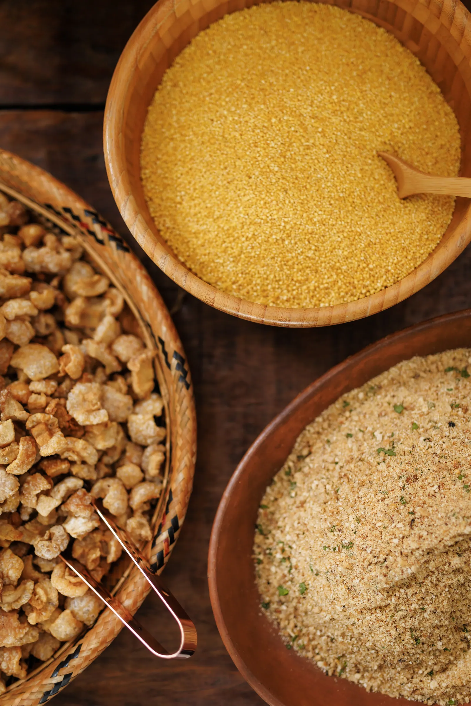 Potes com torresmo crocante, farofa temperada e grãos amarelos finos vistos de cima, ingredientes prontos para o bufê