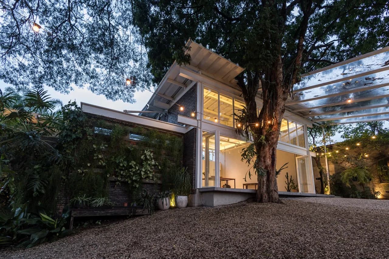 Casa Cósmica ao anoitecer, com a fachada de vidro iluminada entre as árvores
