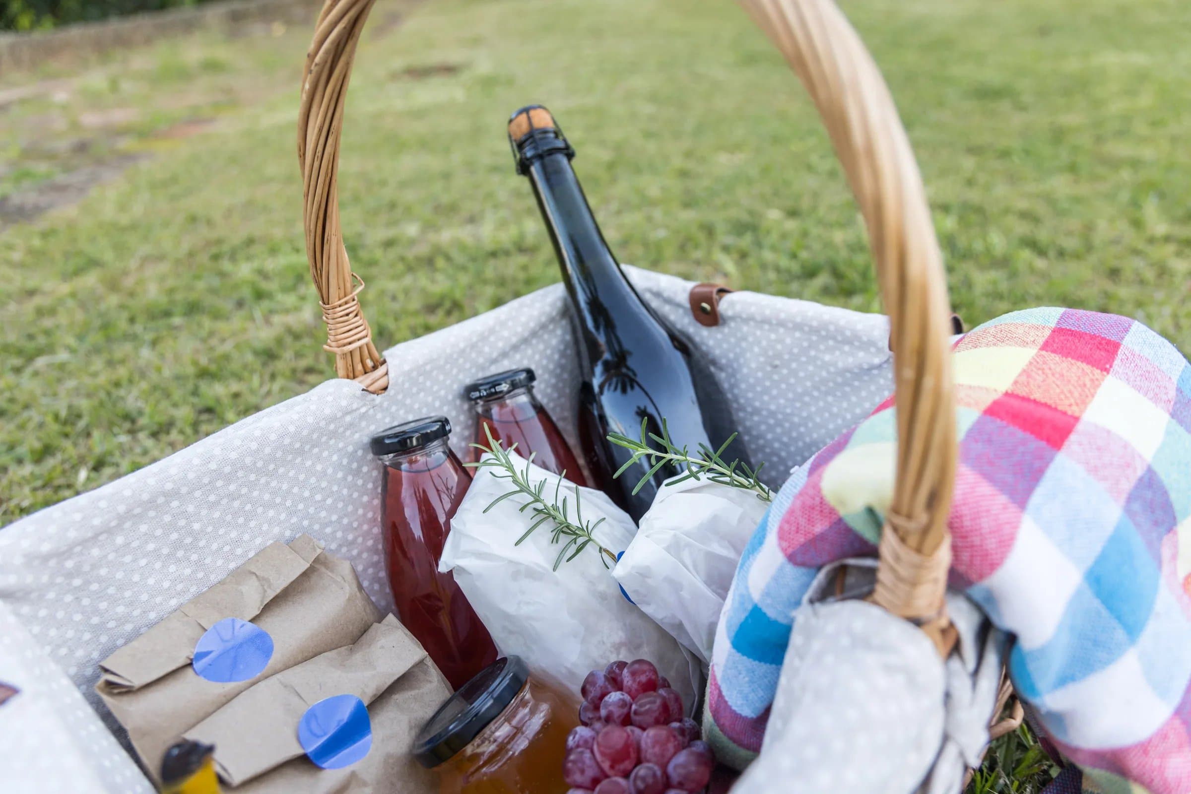 Cesta de piquenique da Cósmica montada em gramado da Fazenda, com pães, queijos, frutas, vinho e mantas para mesa no campo.