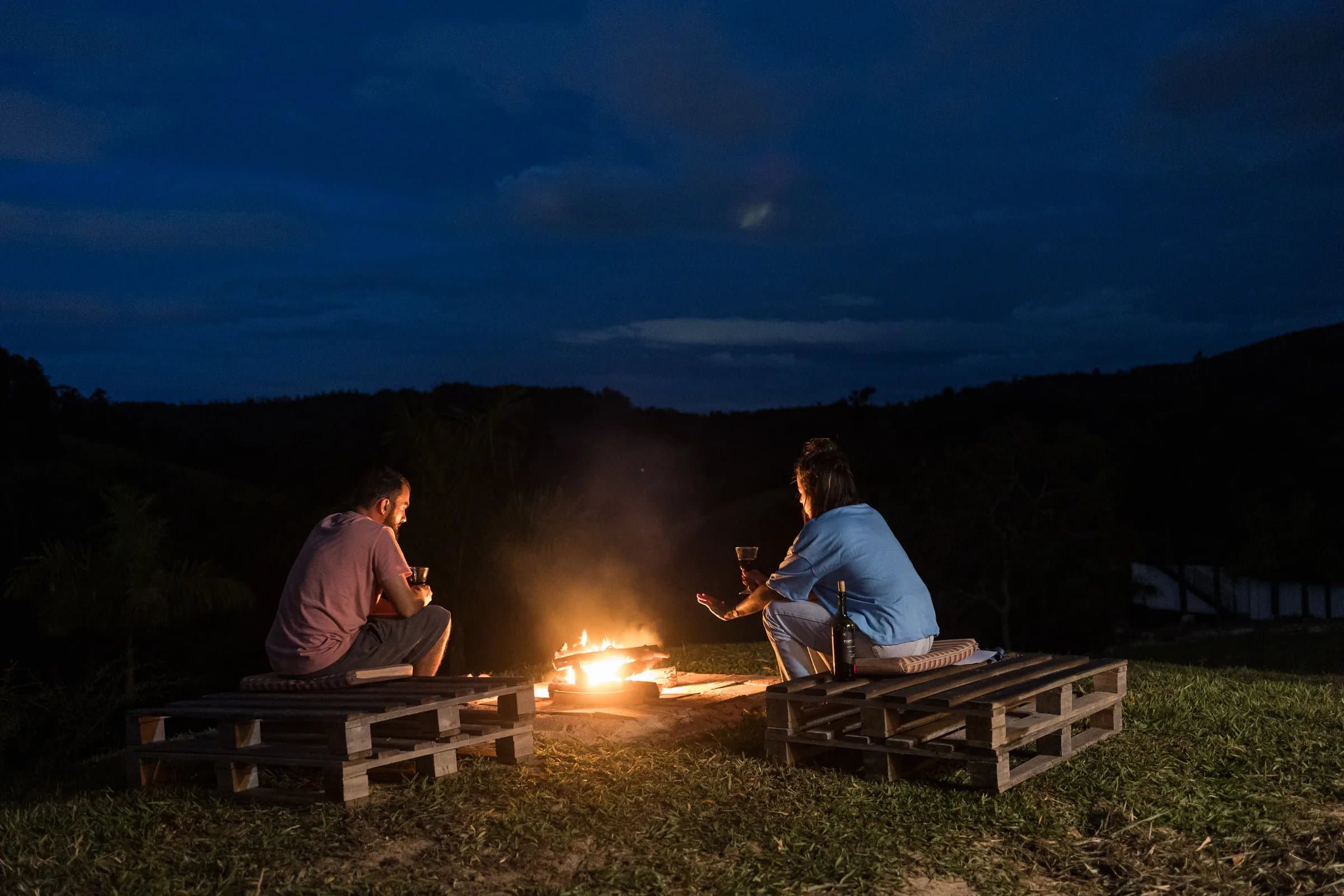 Fogueira acesa em deck de chalé da Fazenda Cósmica, com lenha empilhada e ambiente para reunir hóspedes na noite na Mantiqueira.