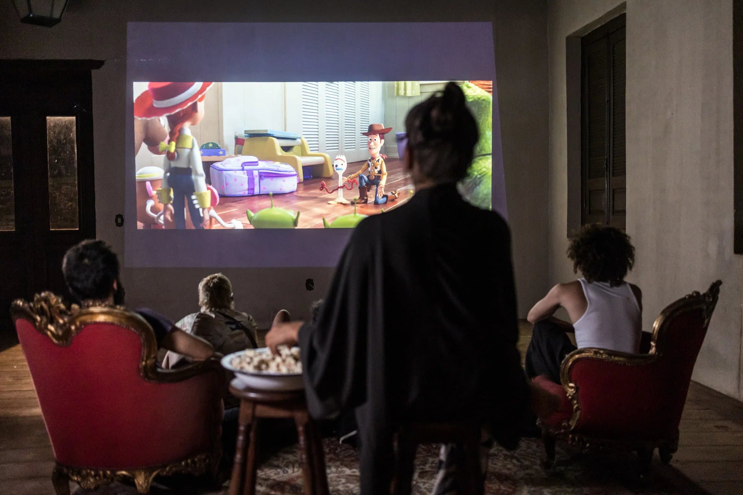 Sessão de cinema na Fazenda Cósmica — projetor na parede com hóspedes acomodados em sofás e poltronas para noite tranquila no chalé.