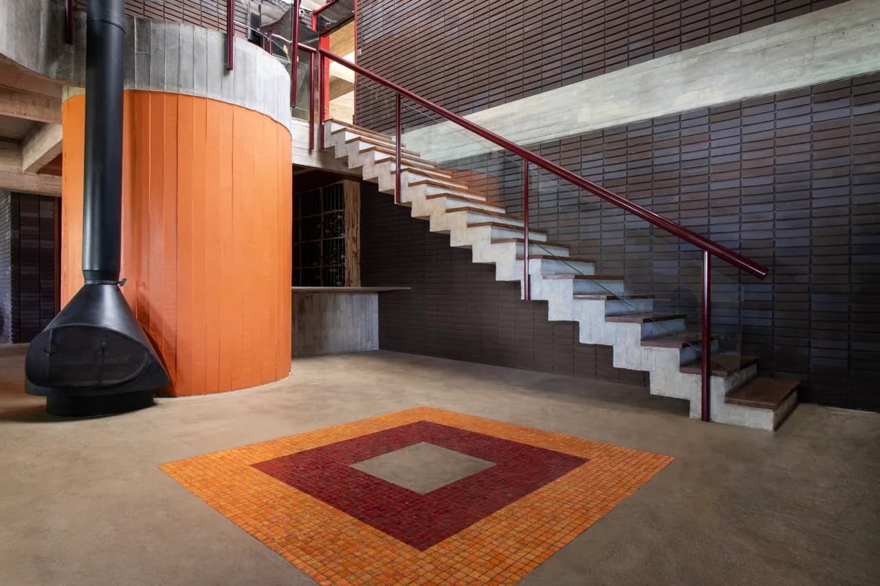 Chaminé preta e escada de corrimão vermelho sobre tapete de mosaico em tons de terracota