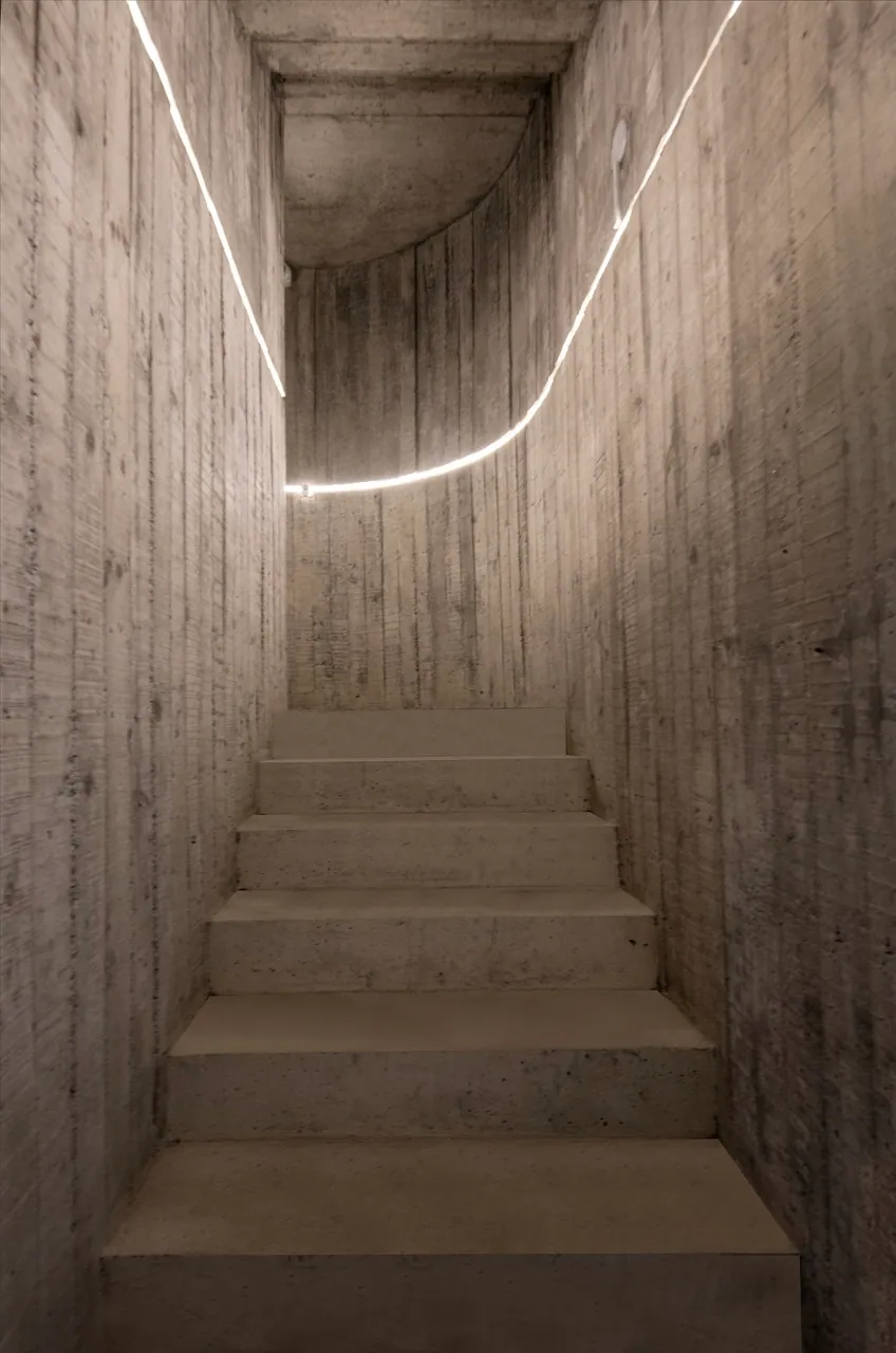 Escada de concreto com fita de luz acompanhando a curva das paredes