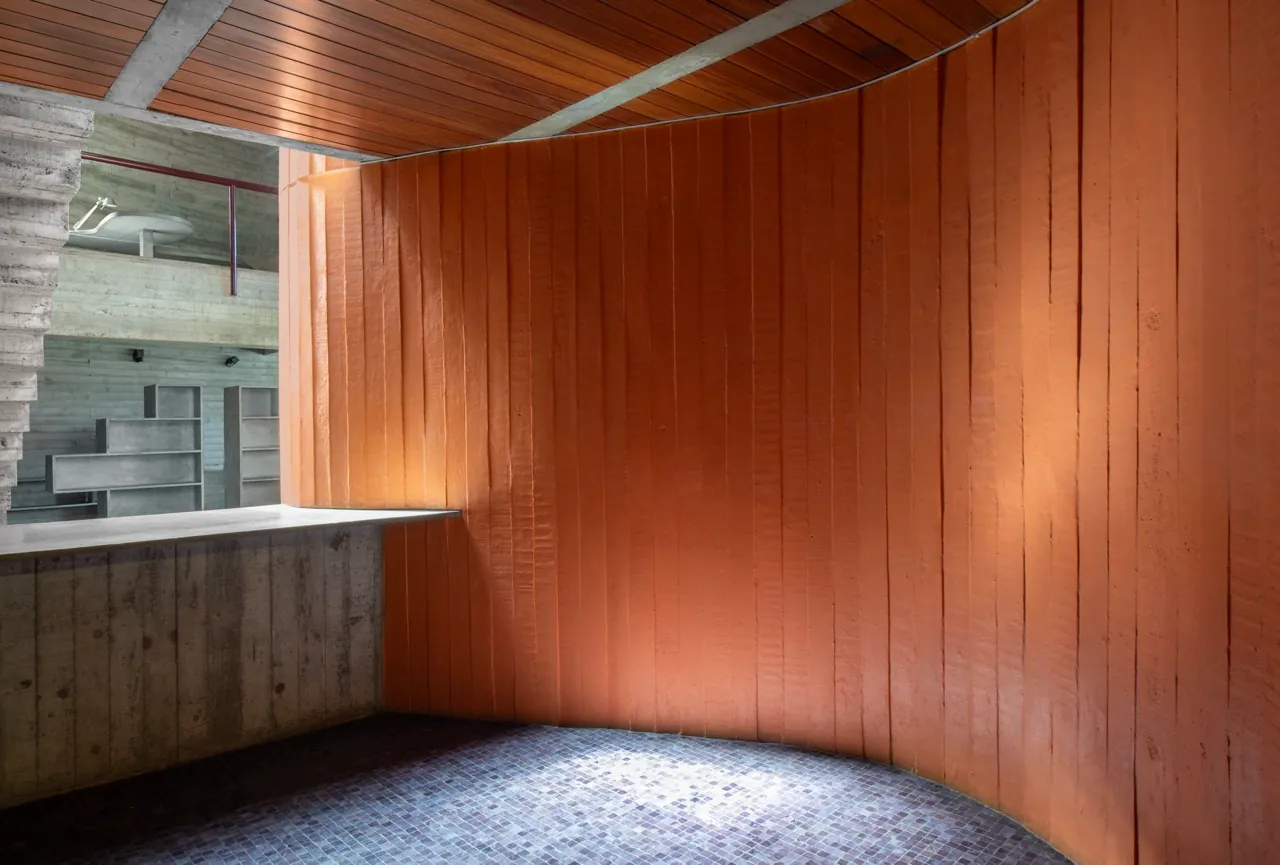 Detalhe da torre curva revestida em madeira laranja, luz baixa sobre o piso de mosaico
