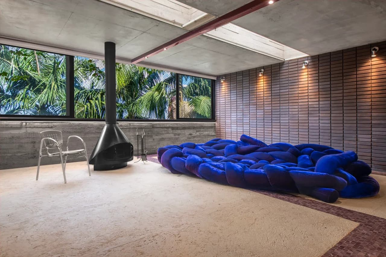 Sofá modular azul profundo em sala de estar com vista para as palmeiras e lareira ao lado
