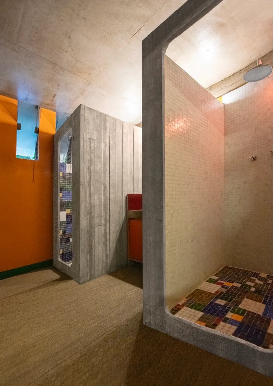 Chuveiros em mosaico colorido do spa da Residência Cósmica, parede laranja ao fundo