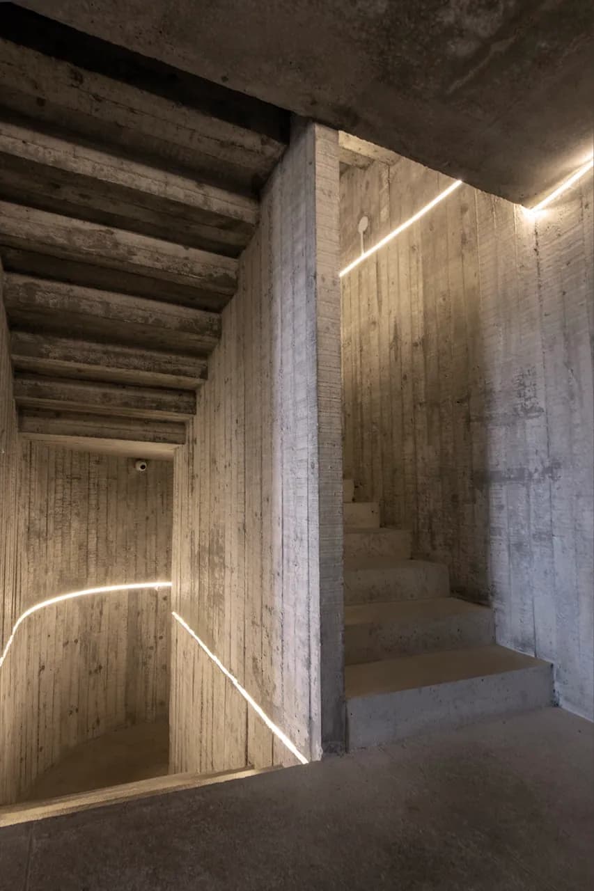 Outro lance da escada de concreto, luz embutida guiando os degraus na penumbra