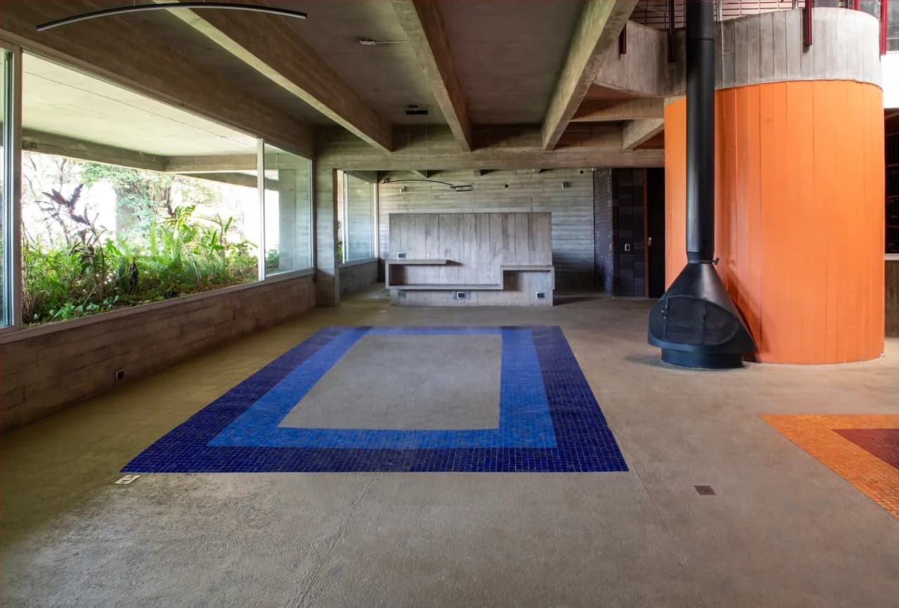 Canto de estar com banco de madeira embutido, tapete de mosaico azul e lareira ao fundo
