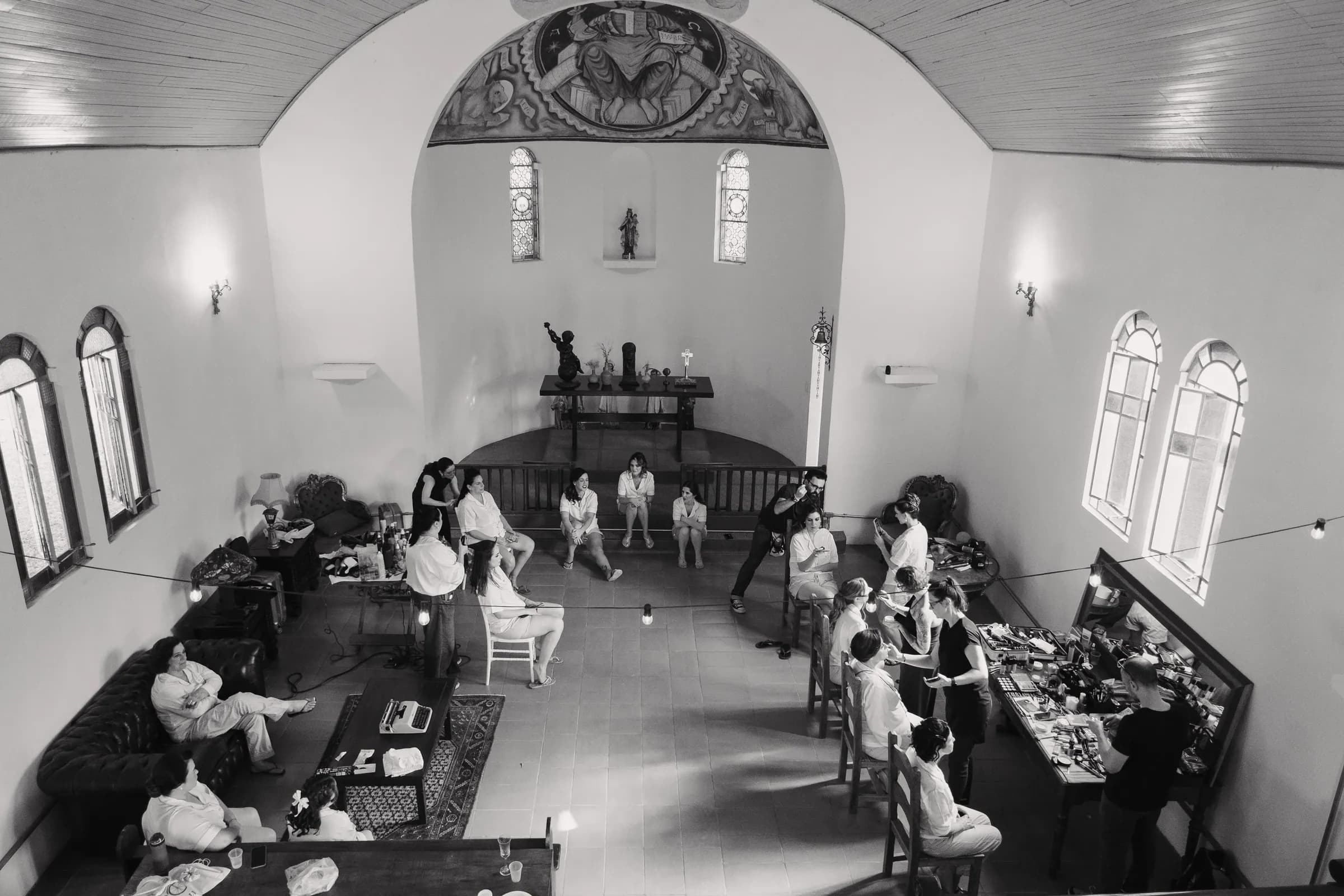 Capela Cósmica transformada em camarim, com um grupo de mulheres se arrumando entre espelhos e vestidos — preparação da noiva e das madrinhas na Fazenda Cósmica
