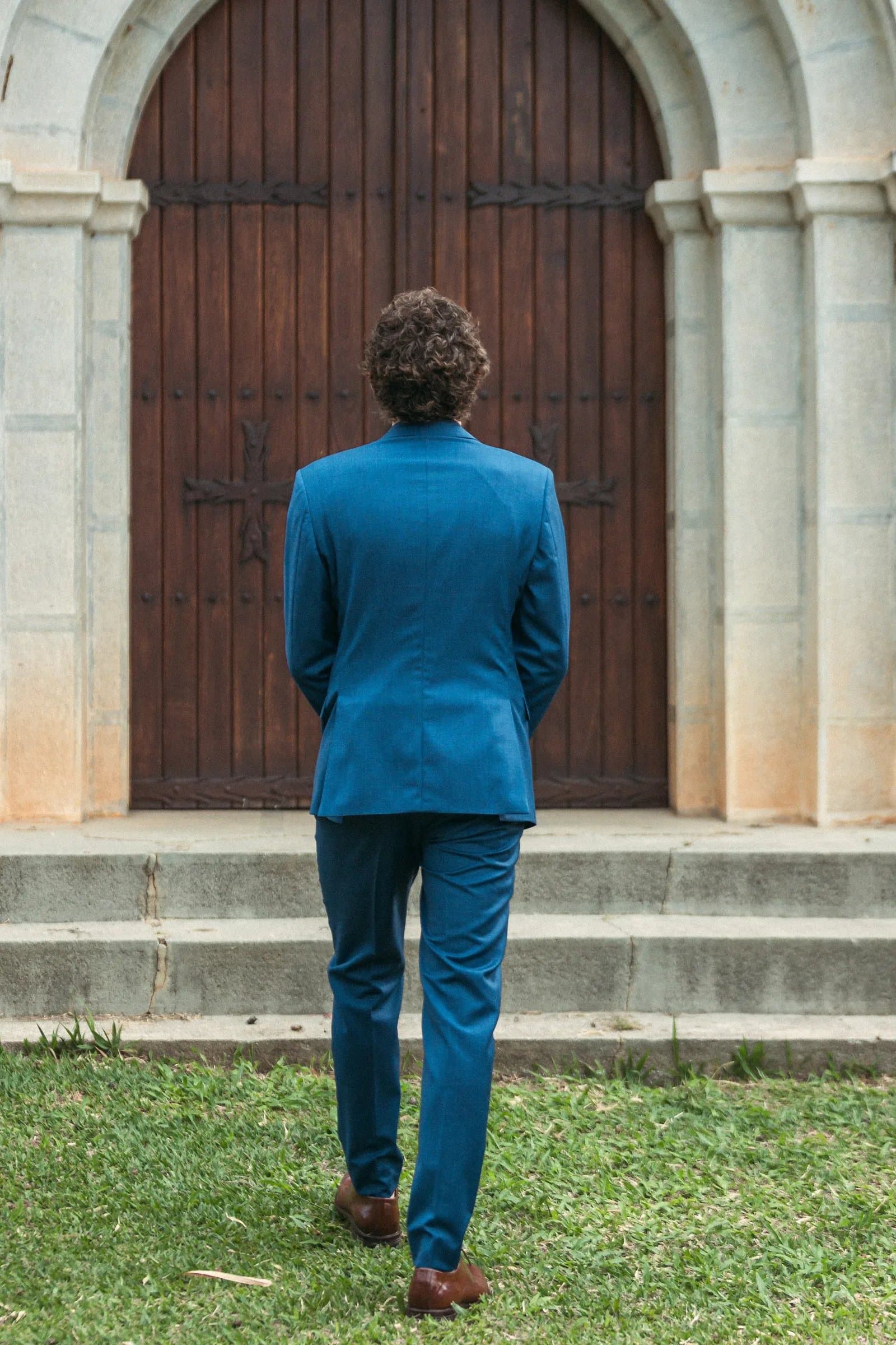 Noivo em terno azul de costas caminhando para a capela em casamento intimista na Fazenda Cósmica
