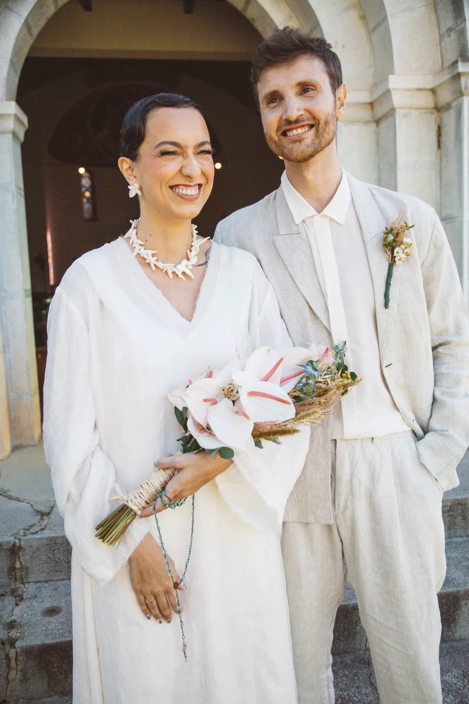 Retrato do casal sorrindo sob o arco de pedra da entrada, à luz do fim de tarde