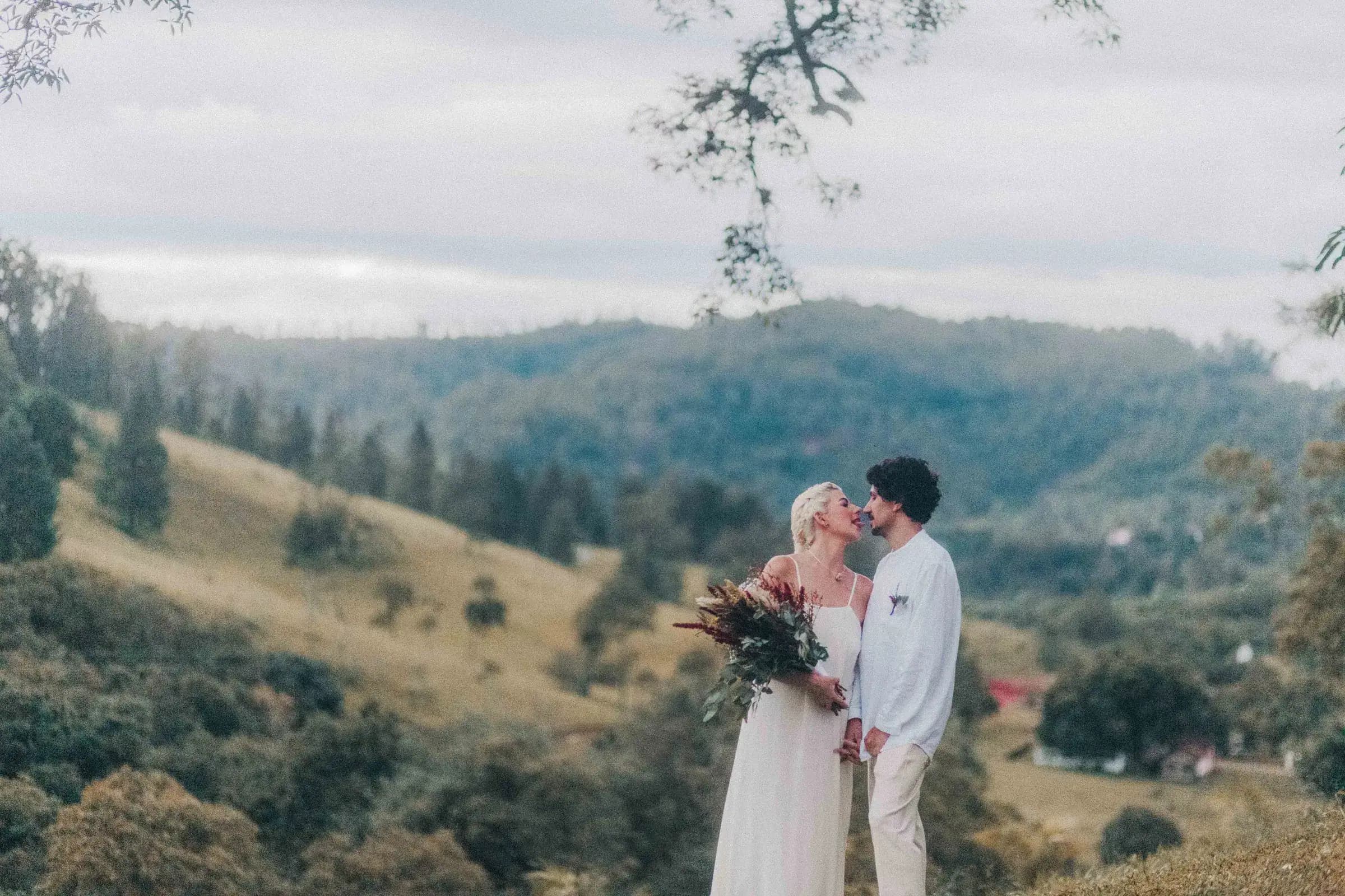 Casal se beijando no alto de um morro da Fazenda Cósmica, com o vale e a serra ao fundo em luz de fim de tarde