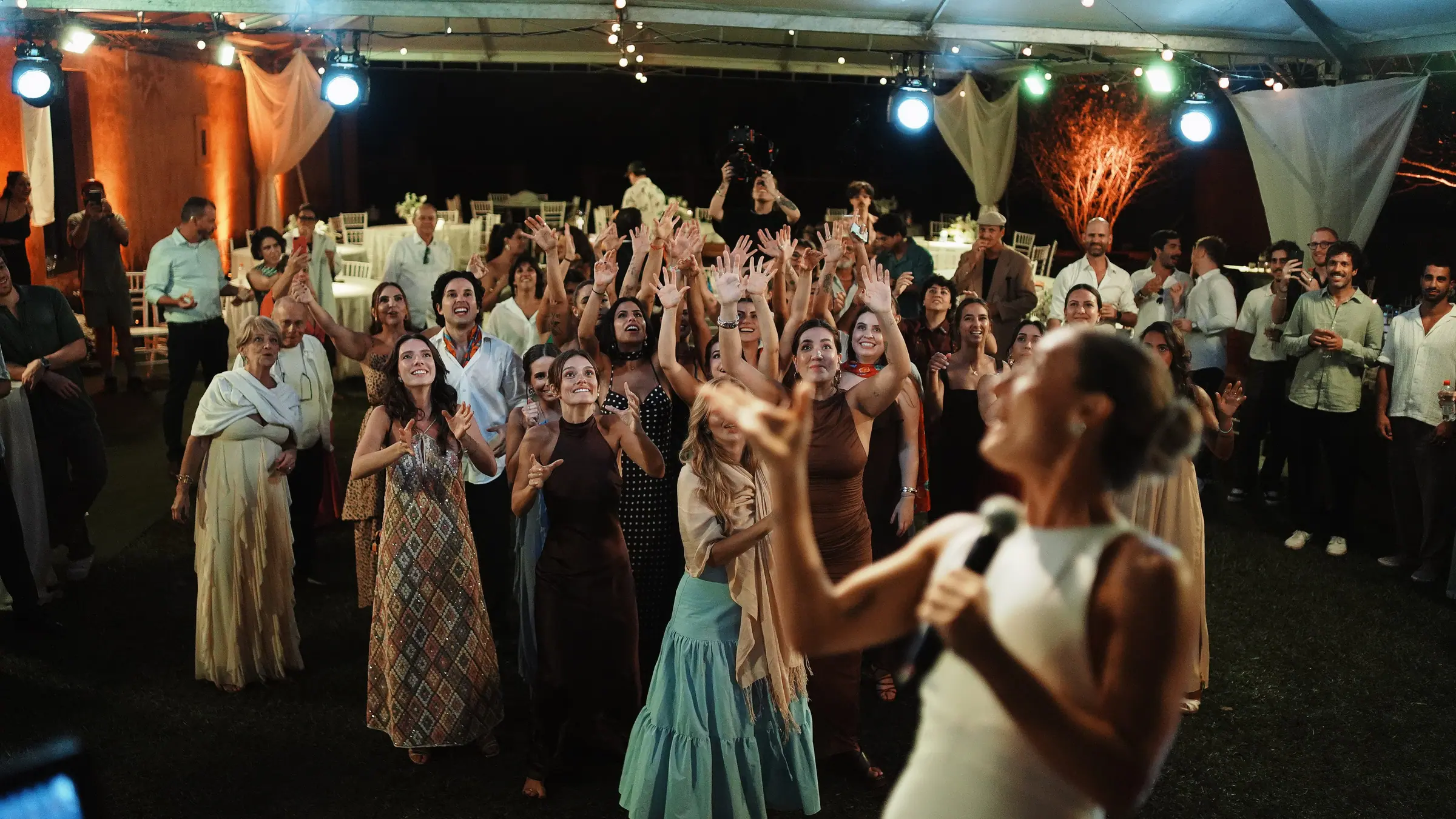 Pista de dança lotada sob a tenda iluminada, com convidados de braços erguidos na Fazenda Cósmica