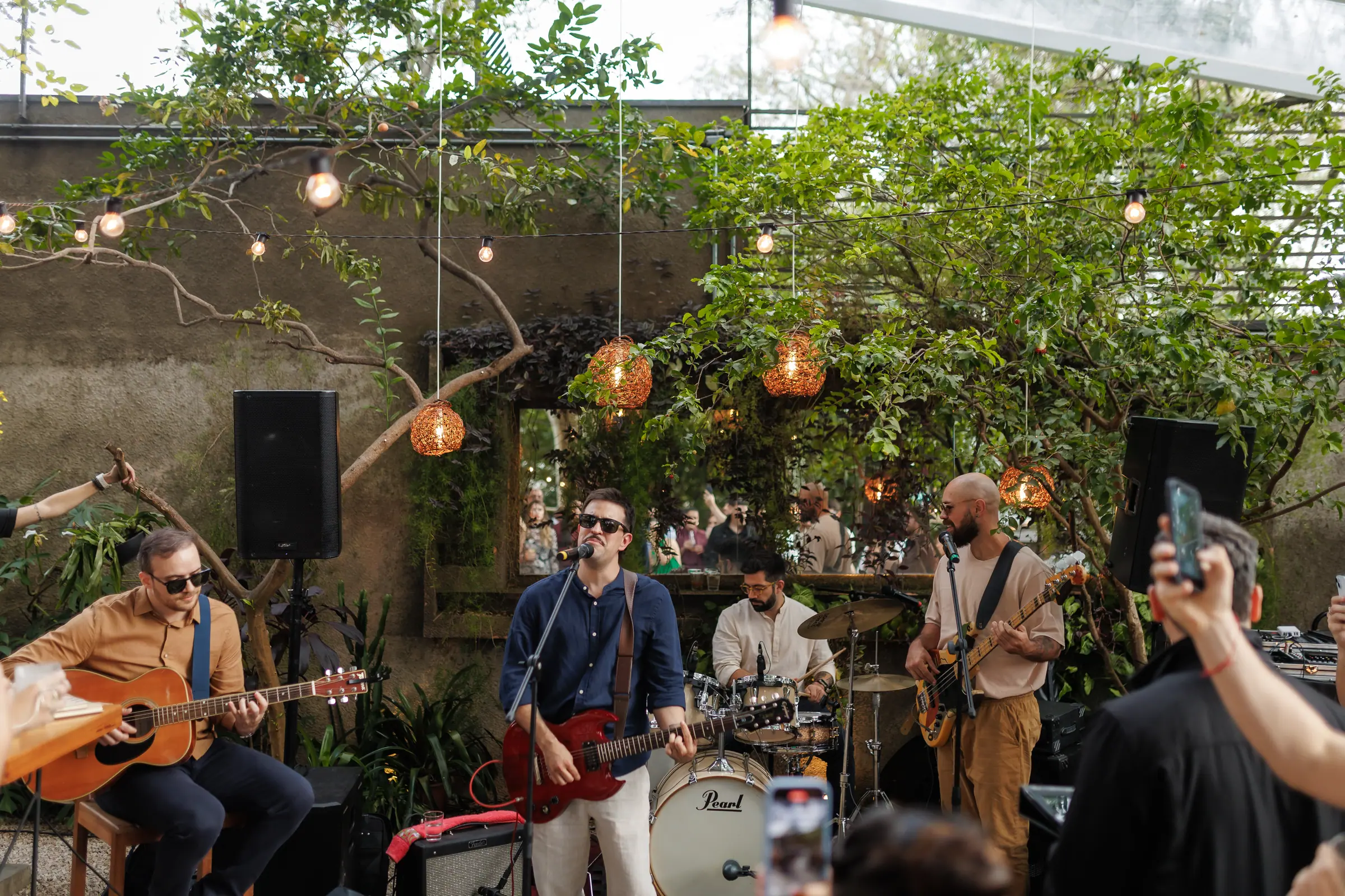 Banda tocando ao vivo na festa de casamento, entre luzes de barbante e a vegetação do jardim