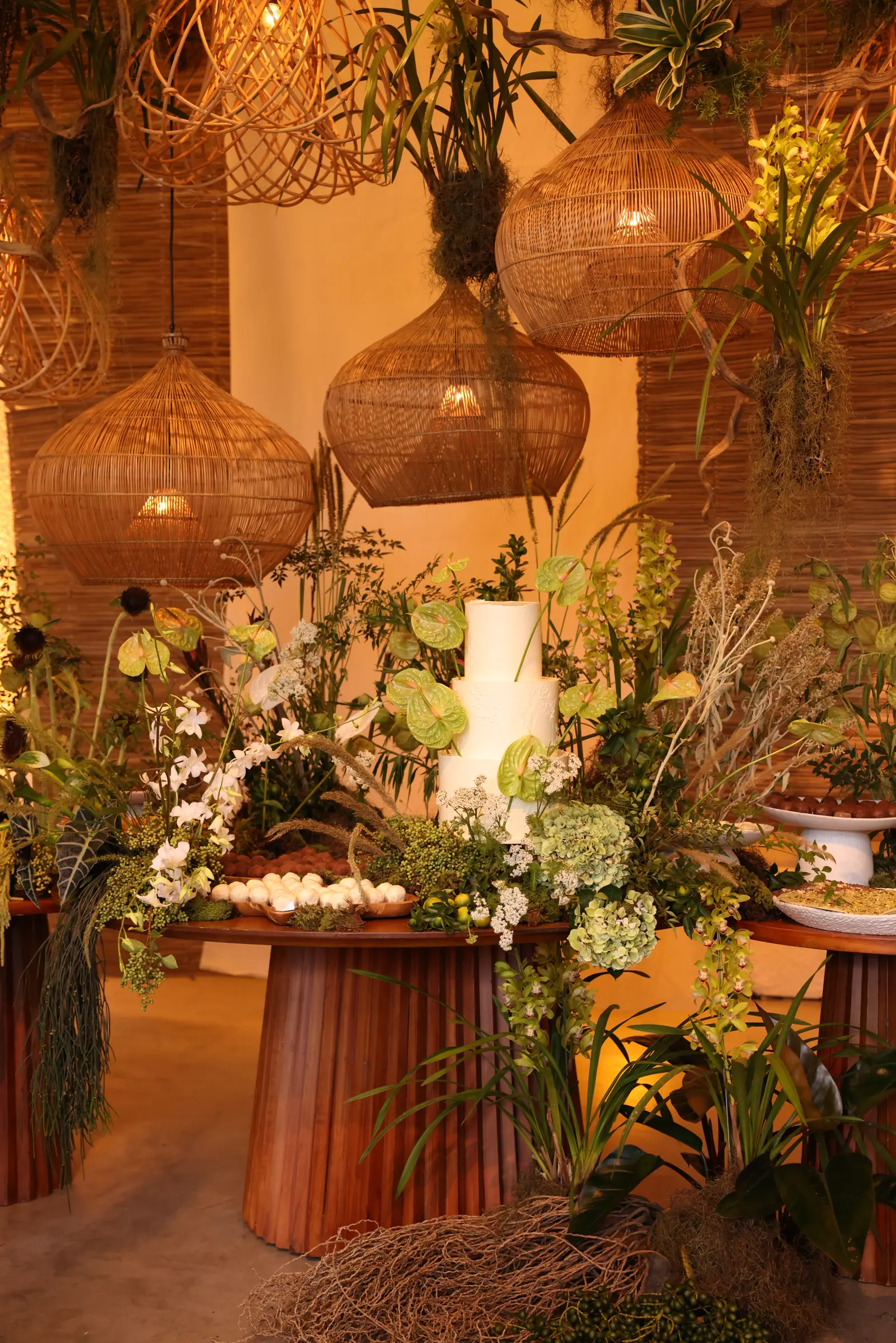 Mesa do bolo de casamento, bolo branco de três andares cercado por antúrios verdes e luminárias de fibra natural
