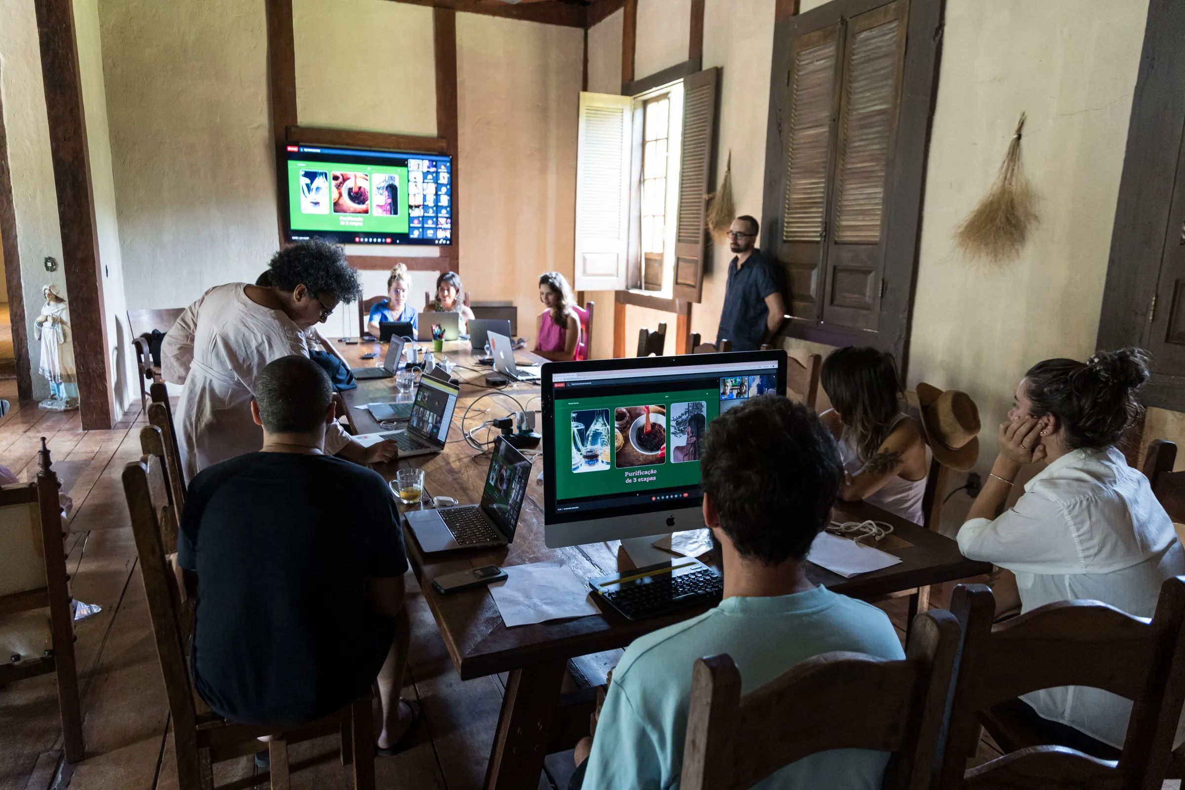 Grupo em workshop dentro do casarão da Fazenda Cósmica, com notebooks e telas, em luz de dia