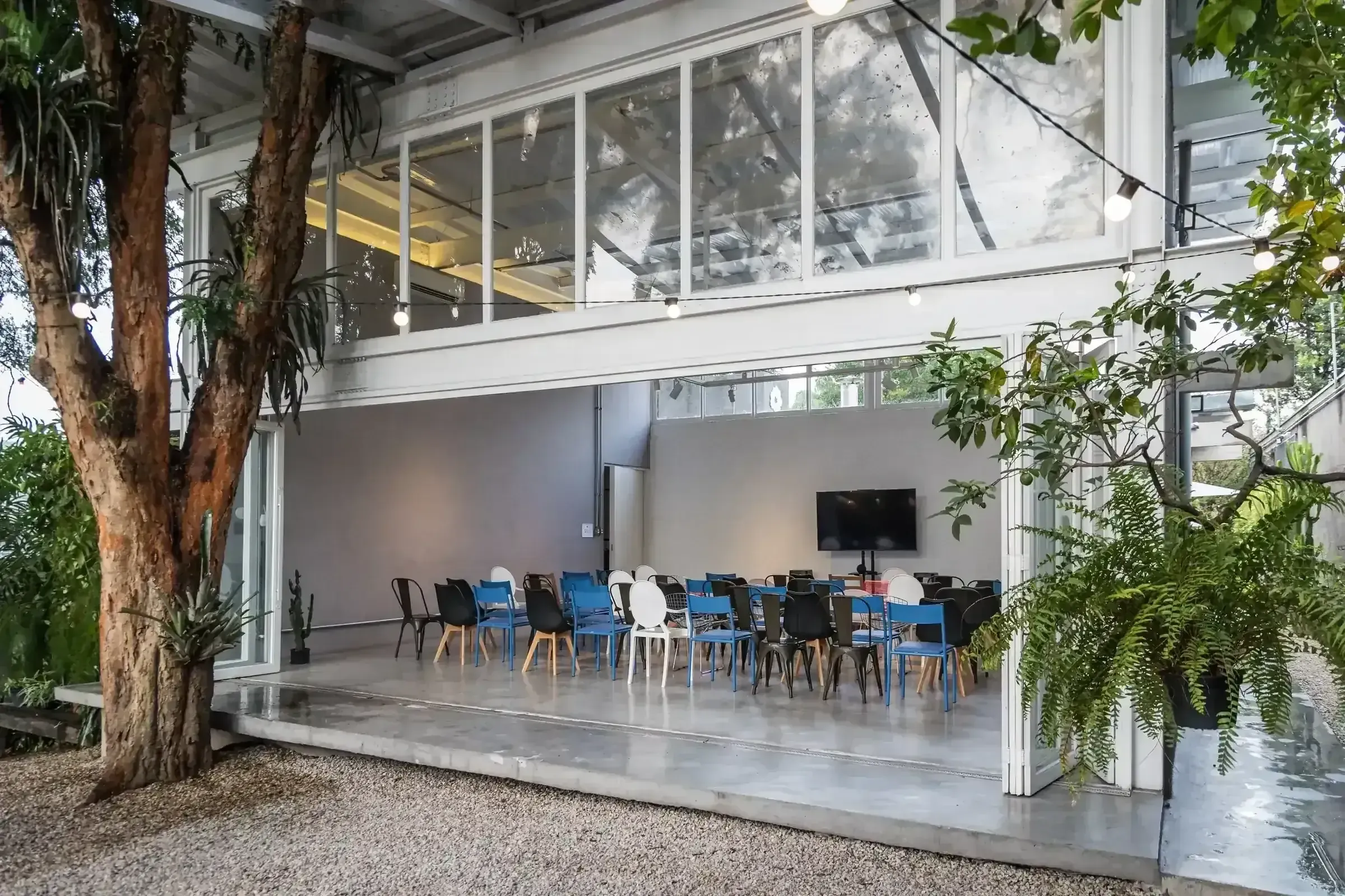 Sala de reunião da Casa Cósmica com tela grande e cadeiras dispostas em roda, plantas penduradas ao fundo