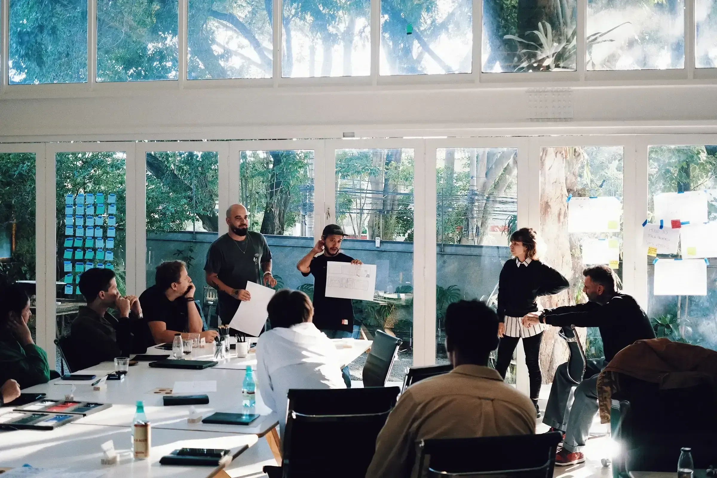 Grupo de profissionais debruçado sobre post-its coloridos numa dinâmica de brainstorming, um deles desenhando num cavalete de madeira