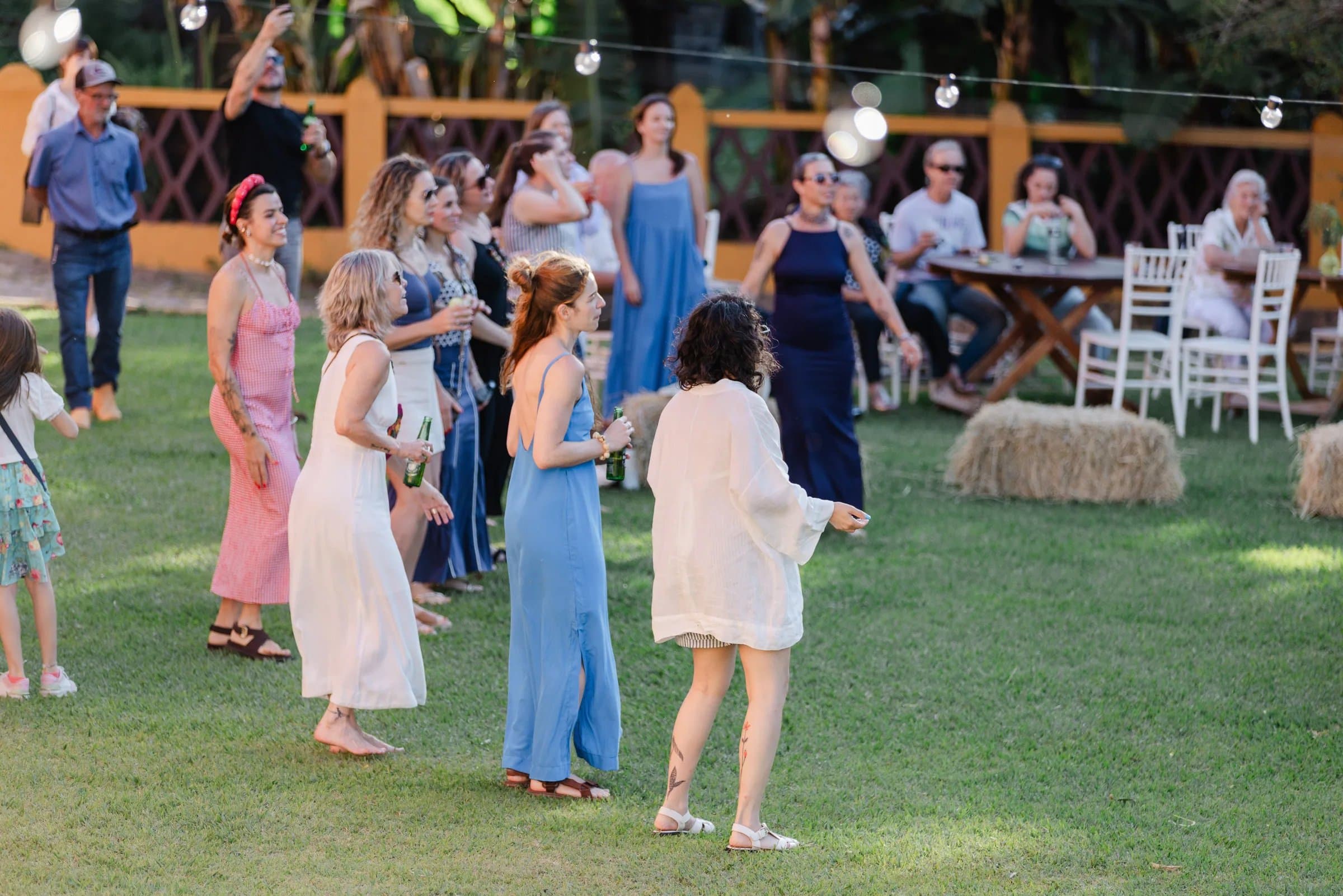 Grupo de amigas e amigos rindo juntos em festa na Fazenda Cósmica, vale verde e mata atlântica desfocados ao fundo, fim de tarde