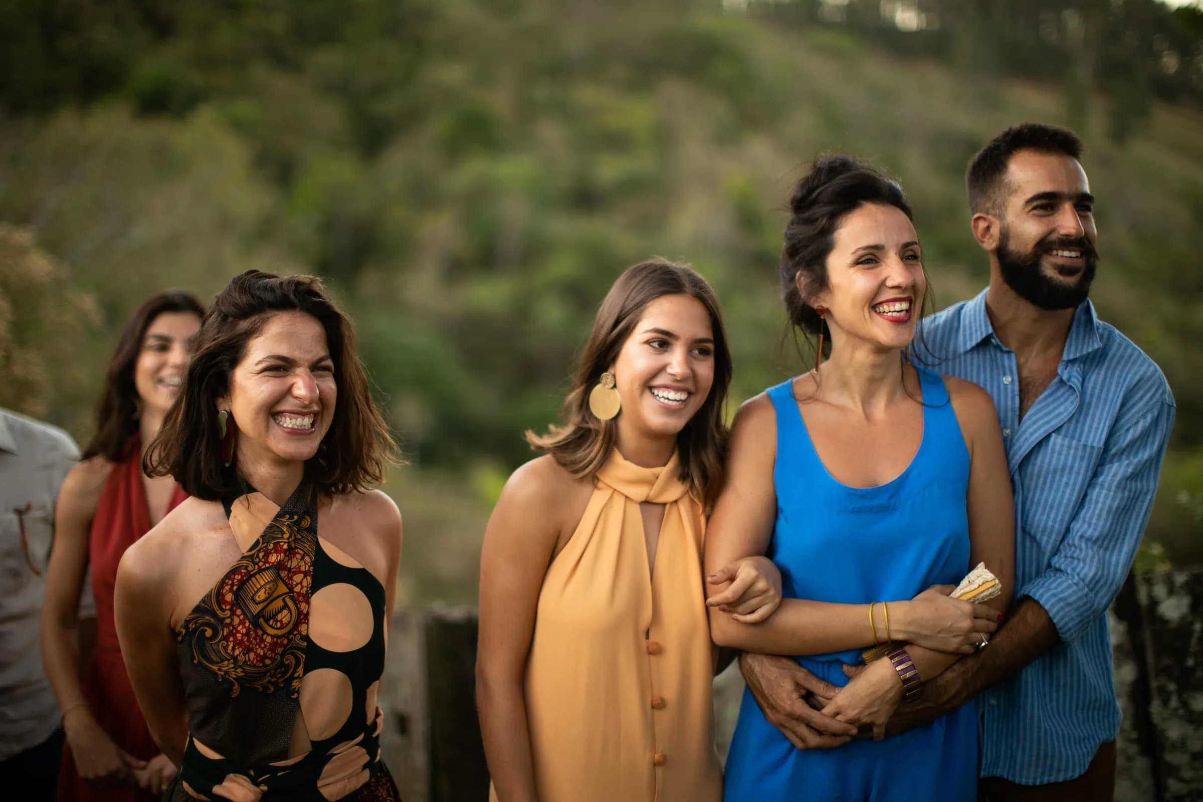 Grupo de amigos rindo juntos em celebração na Fazenda Cósmica, vale verde da Mantiqueira ao fundo no fim de tarde