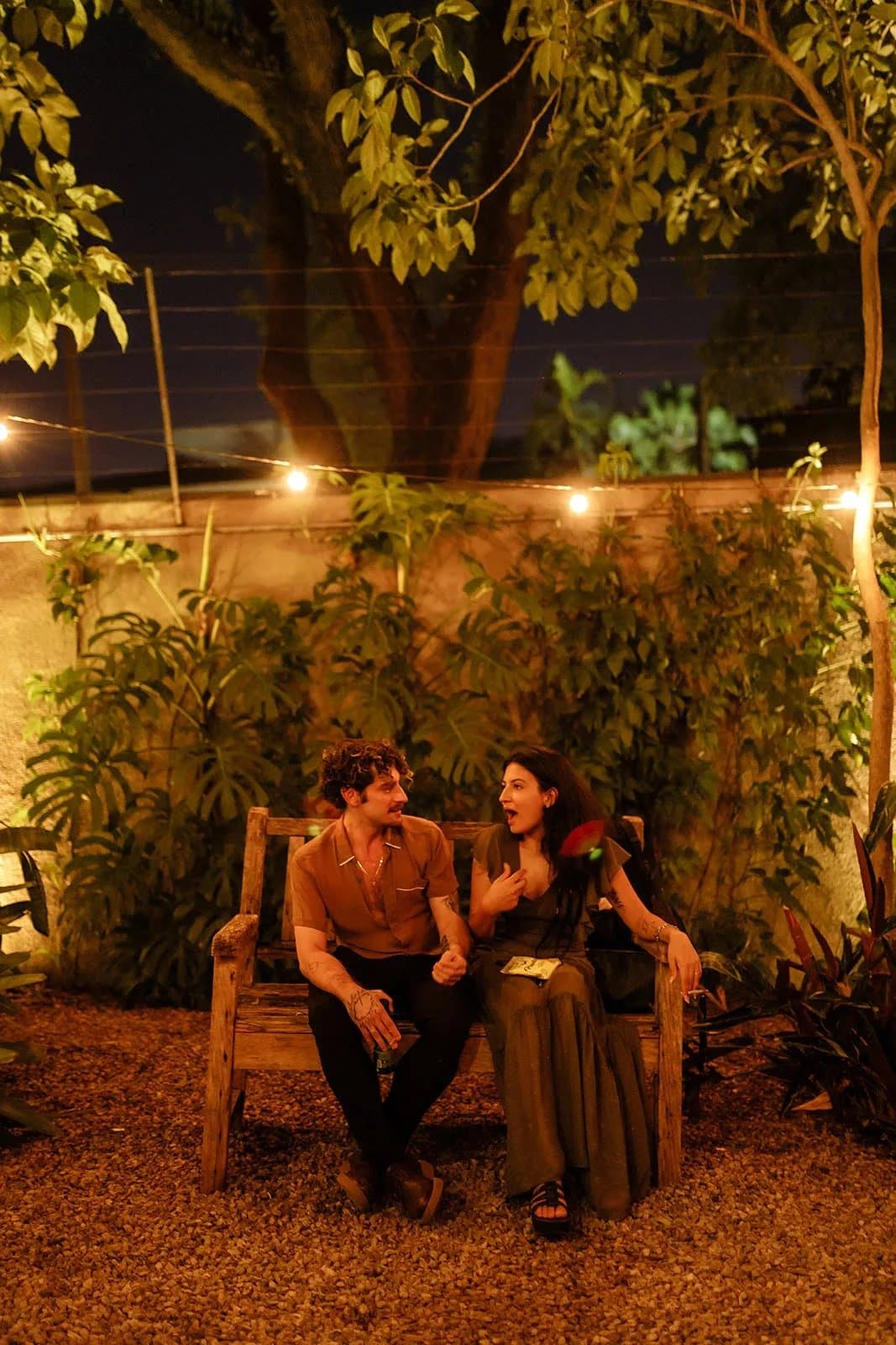 Casal sentado em banco rústico no jardim com plantas e luzes na Casa Cósmica SP em São Paulo